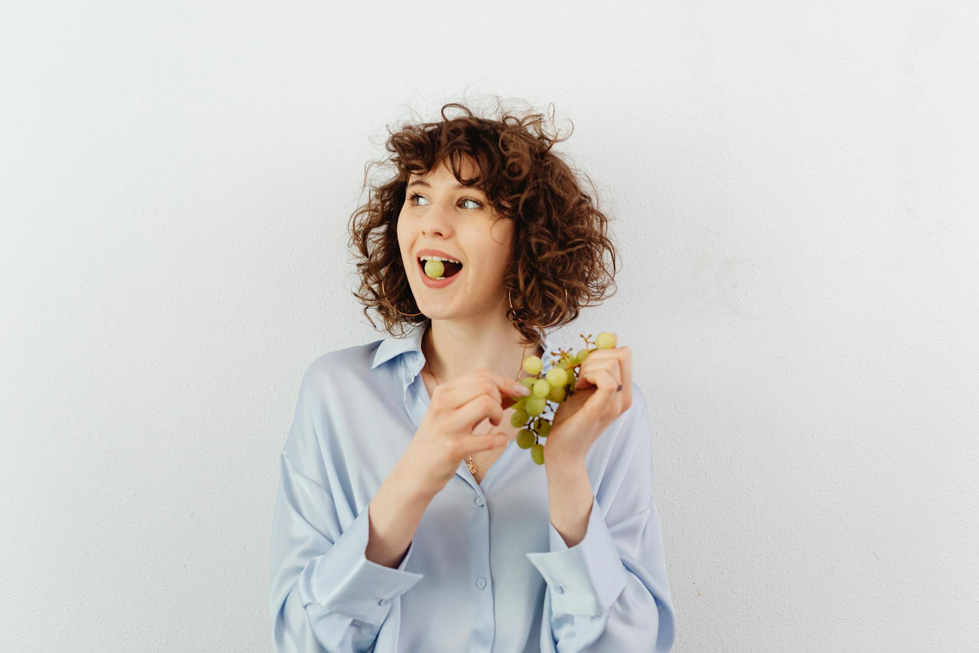 Une femme aux cheveux bouclés mangeant du raisin | Source : Pexels