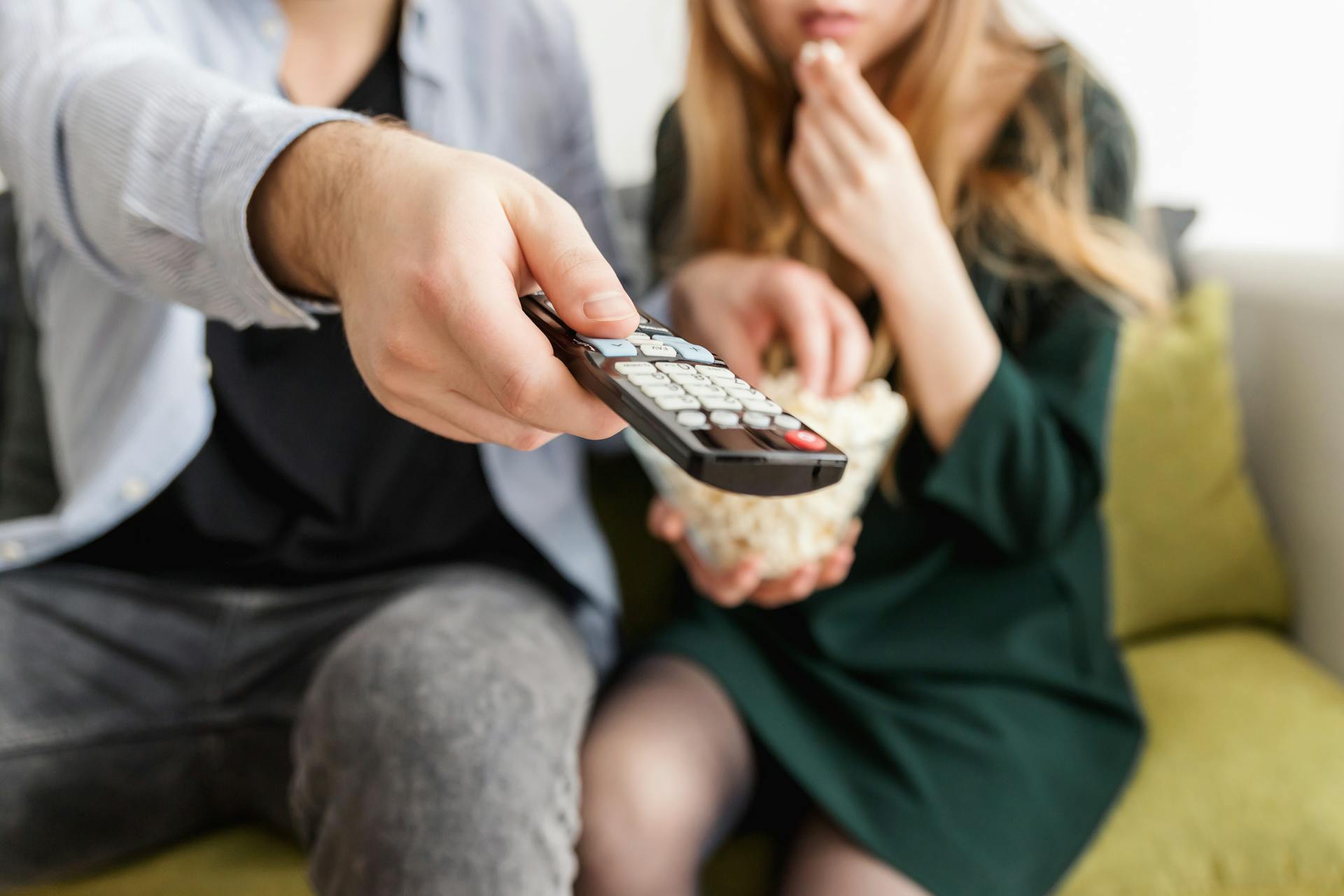 Un homme tenant une télécommande tout en mangeant du pop-corn avec sa femme | Source : Pexels