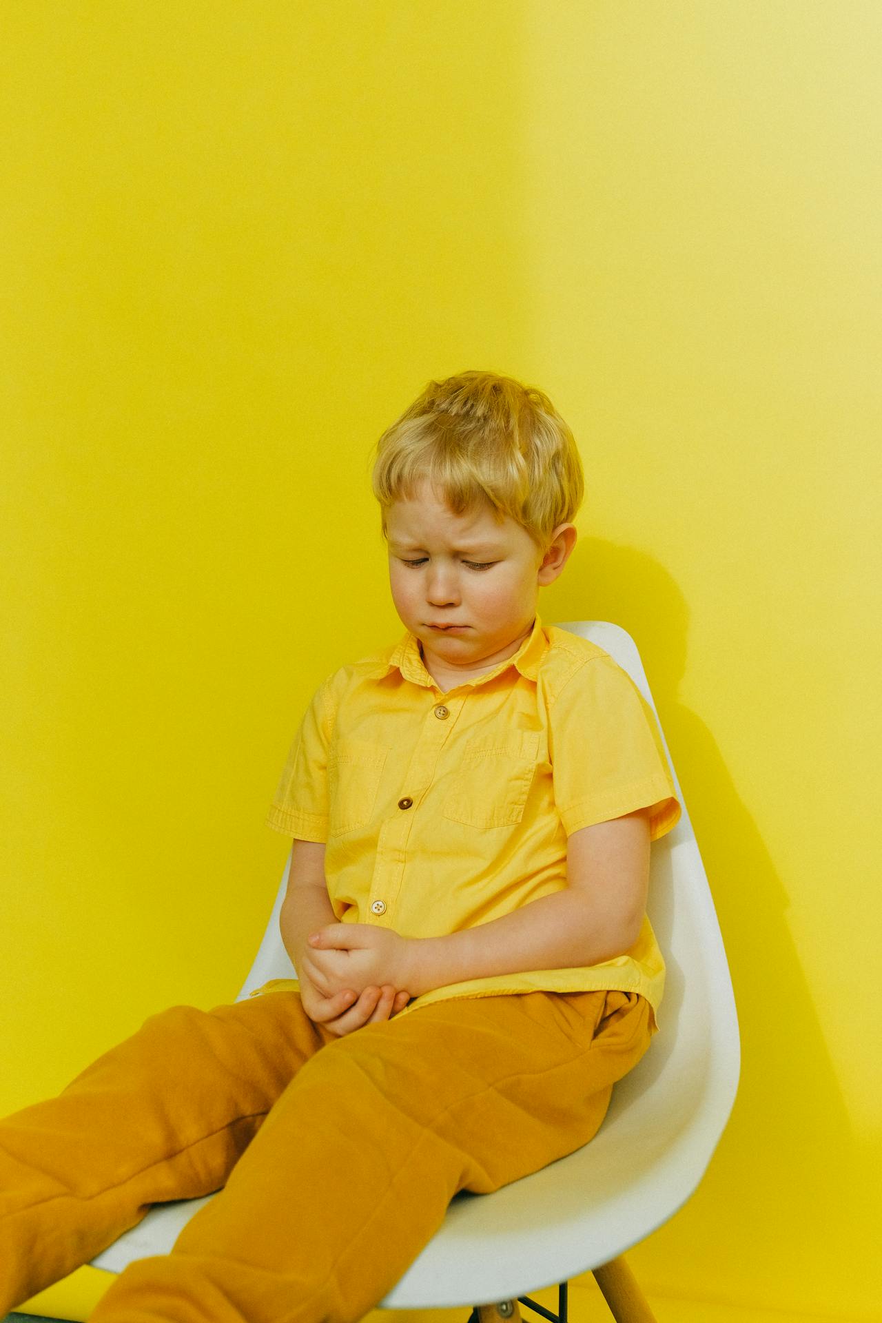Un petit garçon triste assis sur une chaise | Source : Pexels