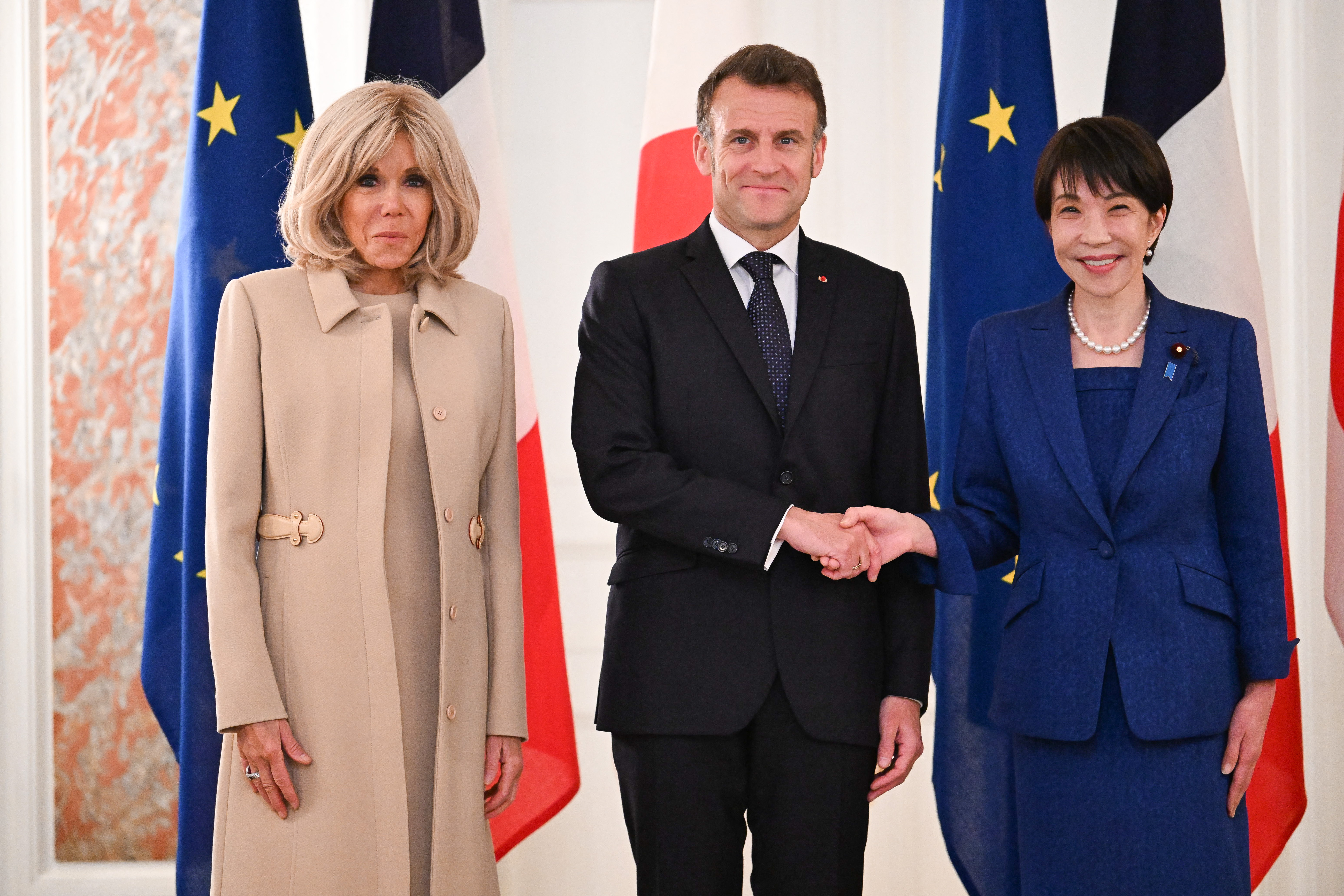 Le président français Emmanuel Macron (au centre) serre la main de la Première ministre japonaise Sanae Takaichi sous le regard de son épouse Brigitte Macron (à gauche), lors d'une cérémonie de bienvenue au palais d'Akasaka à Tokyo, le 1er avril 2026 I Source : Getty Images