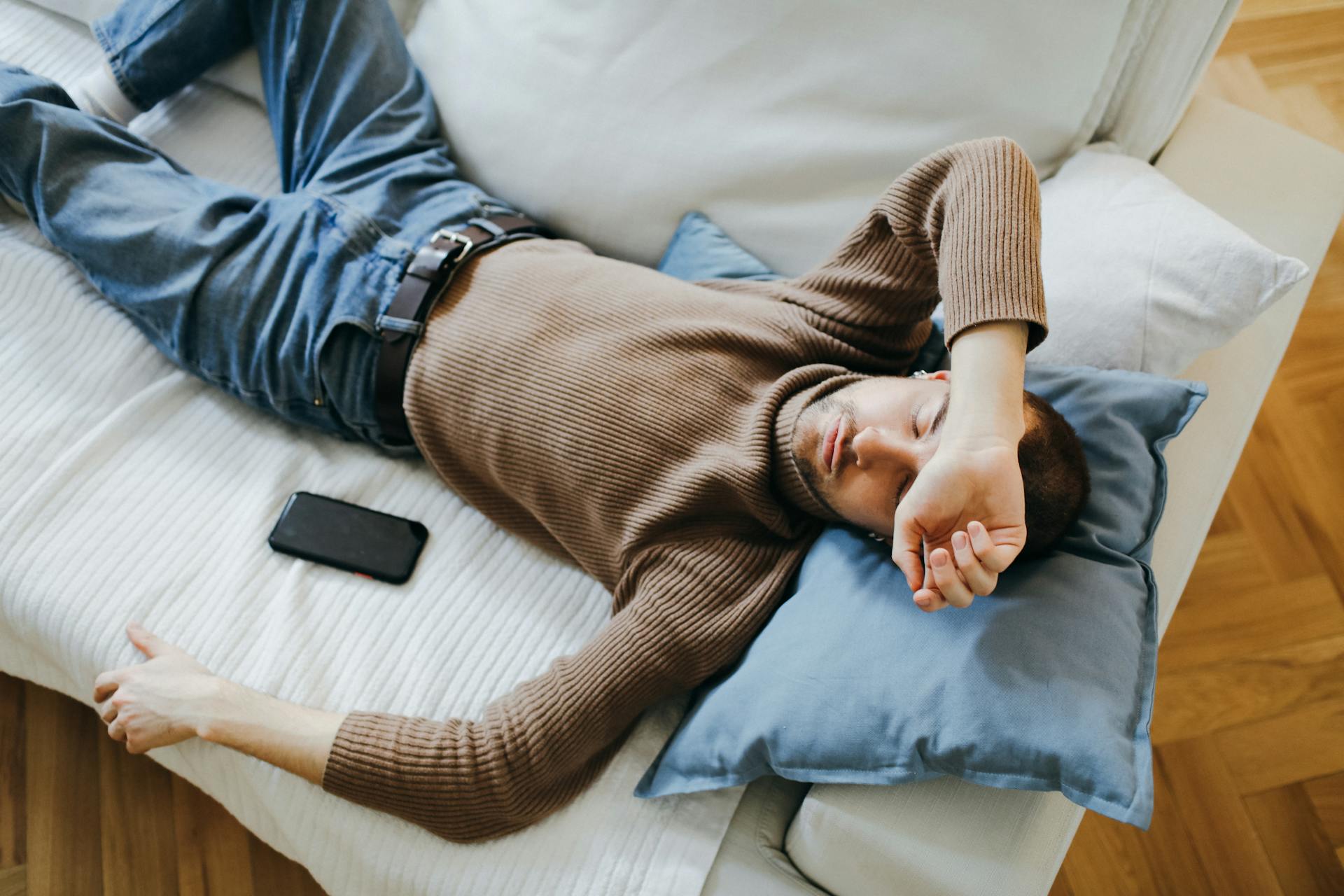 Un homme dormant sur le canapé avec son téléphone à côté de lui | Source : Pexels