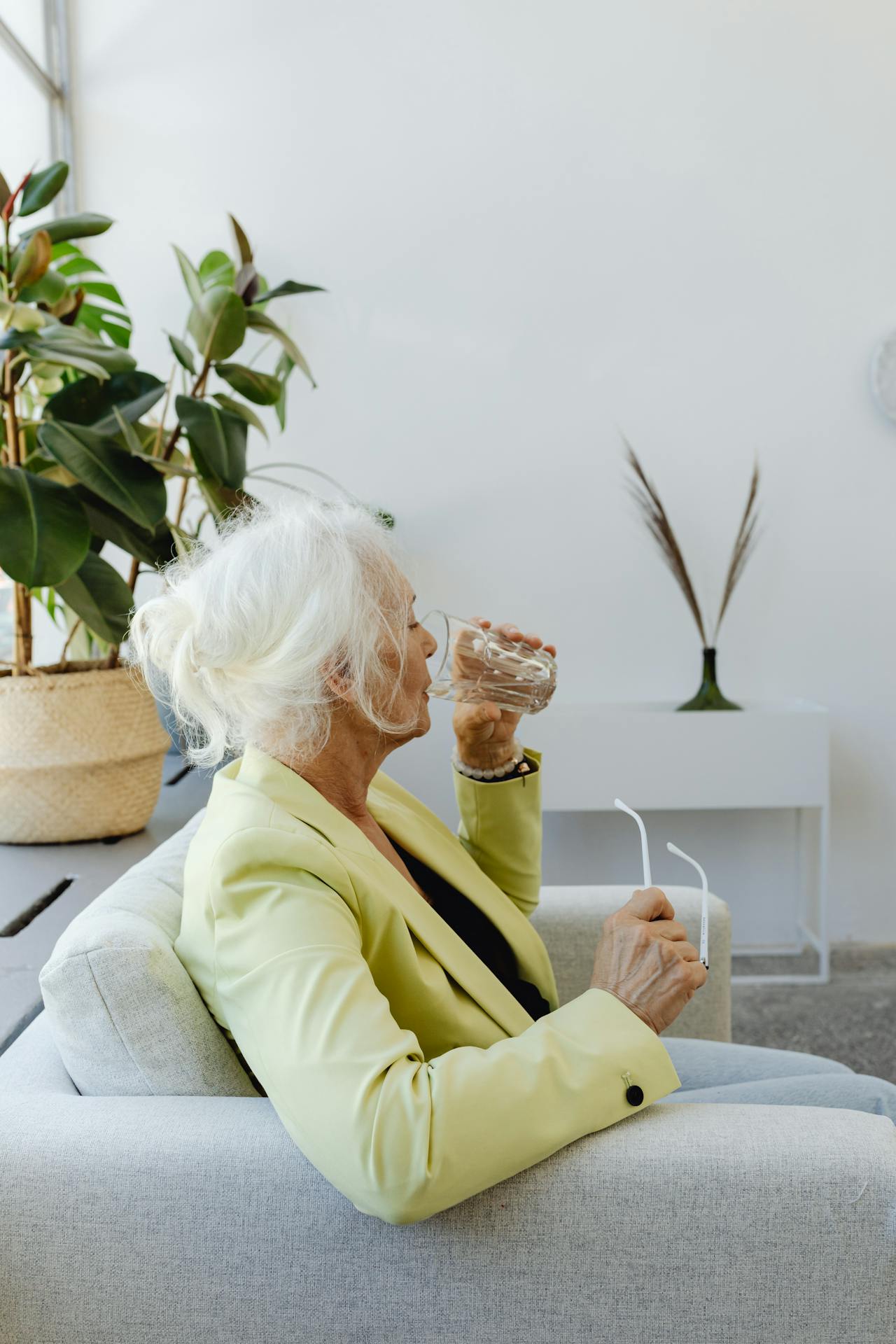 Une femme âgée assise sur le canapé et buvant un verre d'eau | Source : Pexels