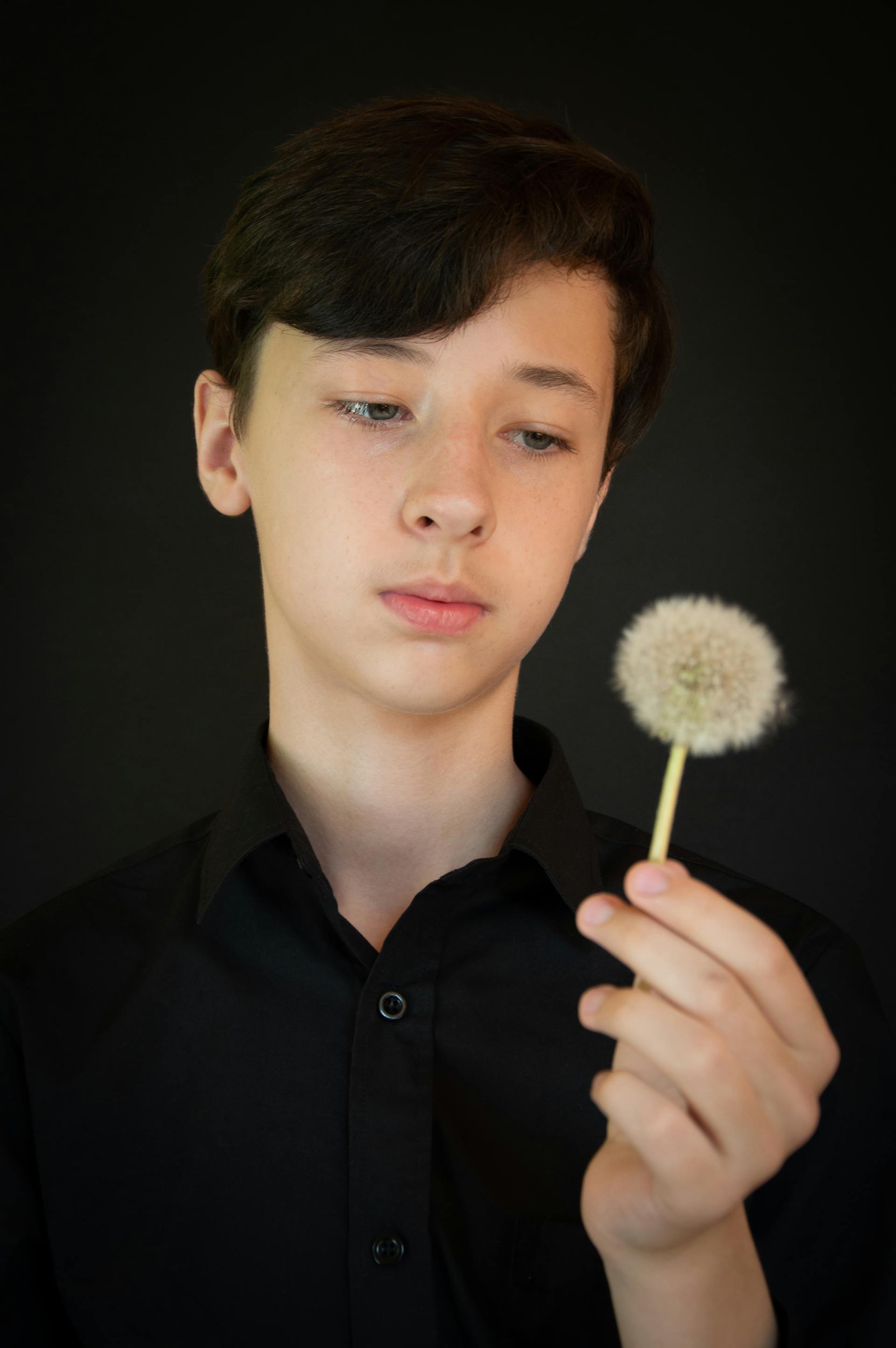 Un adolescent qui regarde un pissenlit dans sa main | Source : Pexels