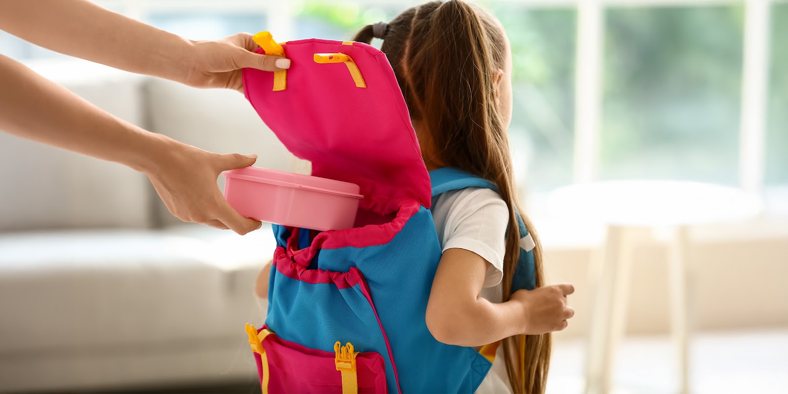Un adulte qui place une boîte à lunch dans le sac à dos d'un enfant | Source : Shutterstock
