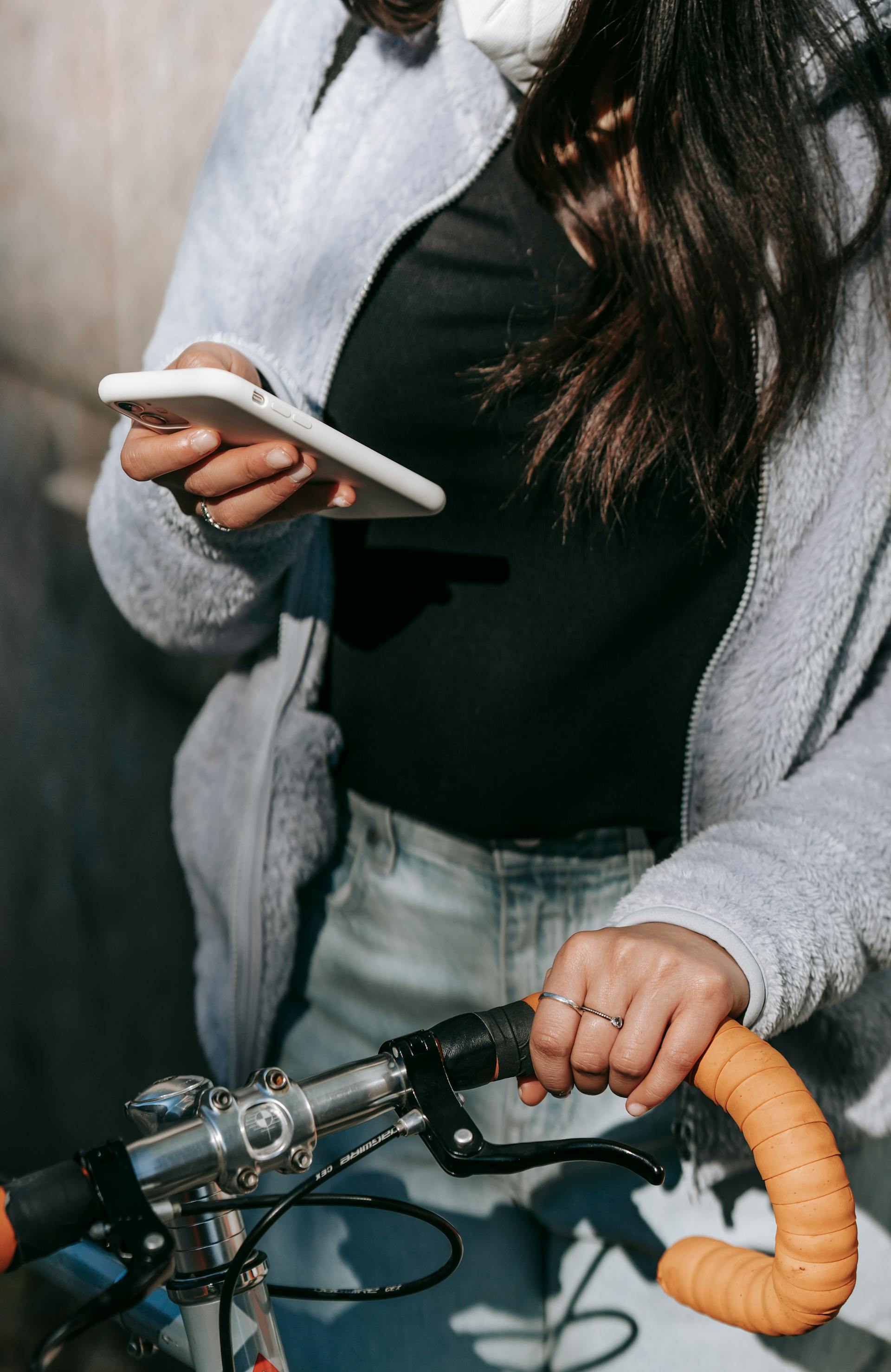 Une jeune femme utilise son téléphone tout en tenant la poignée de son vélo | Source : Pexels