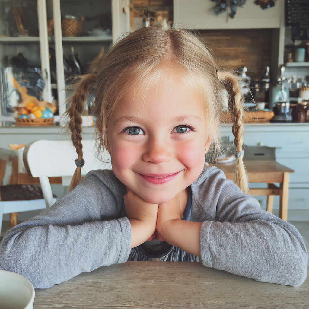 Une petite fille souriante assise à la table du petit déjeuner | Source : Midjourney