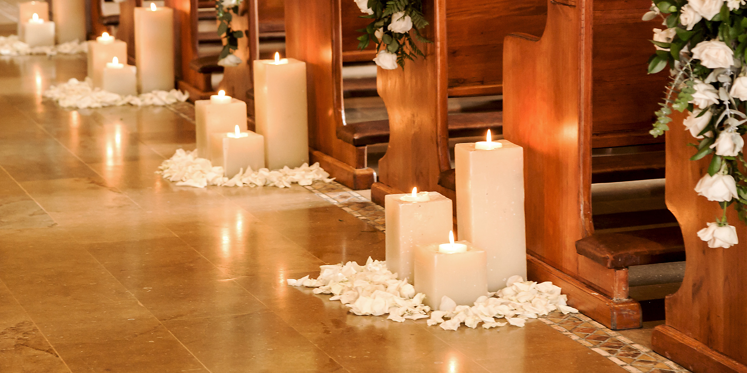De douces bougies bordent l'allée, parsemée de pétales de roses blanches et encadrée par des bancs en bois | Source : Shutterstock