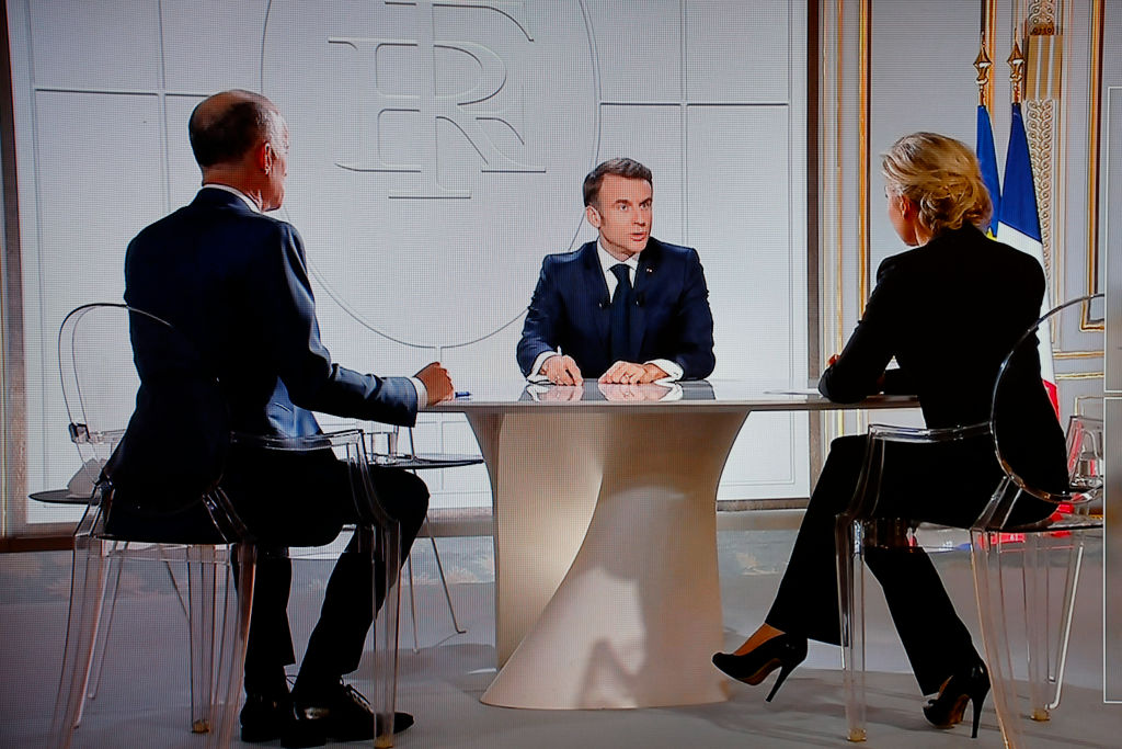 Cette photographie prise le 14 mars 2024 montre un écran de télévision diffusant le président français Emmanuel Macron (C) s'adressant à une interview en direct sur les chaînes de télévision françaises TF1 et France 2 avec l'animateur et journaliste de TF1 Gilles Bouleau (G) et l'animatrice et journaliste de France Télévisions Anne-Sophie Lapix (D), au palais présidentiel de l'Élysée à Paris I Source : Getty Images