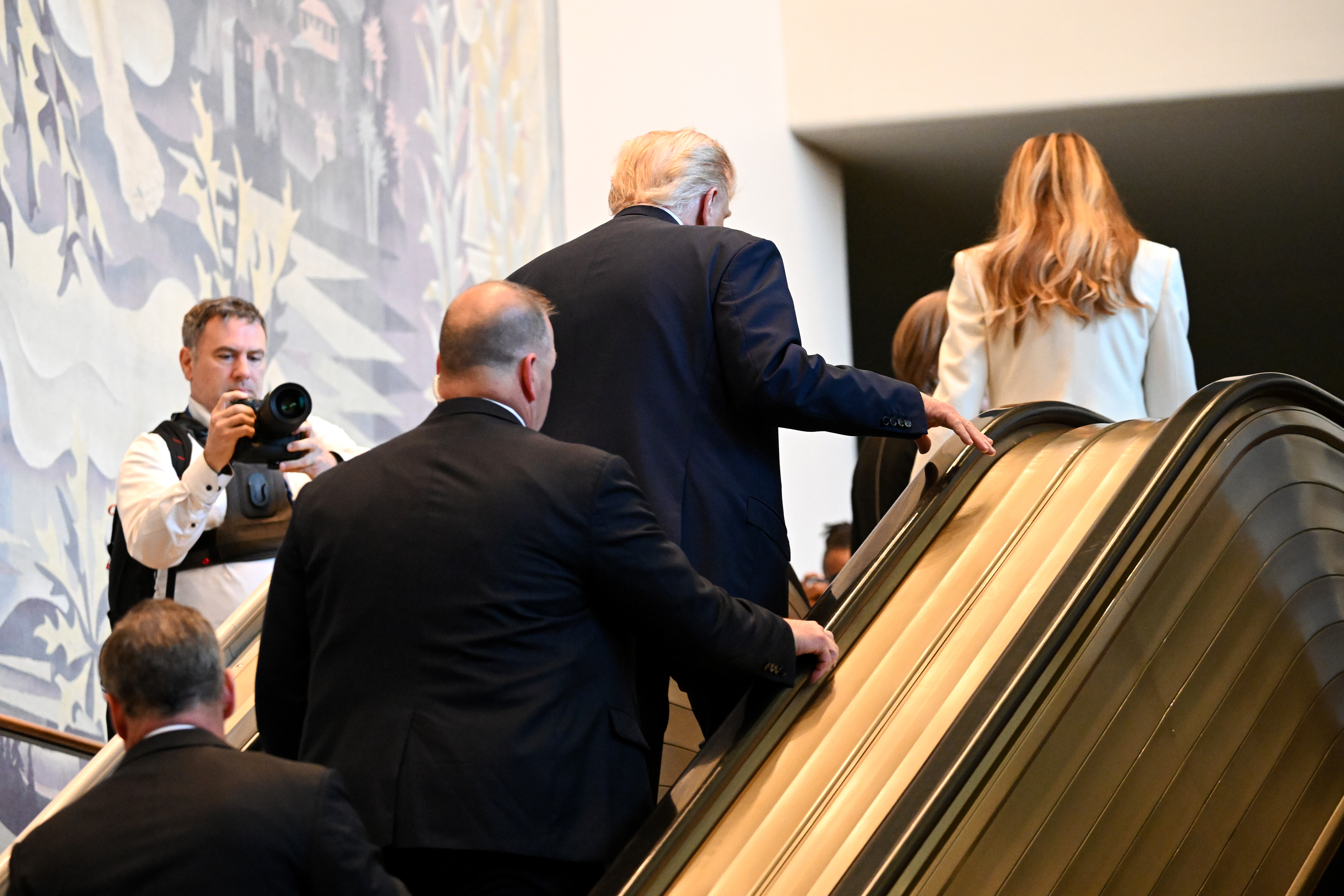 Donald et Melania Trump en haut de l'escalator avec la délégation américaine qui suit derrière. | Source : Getty Images