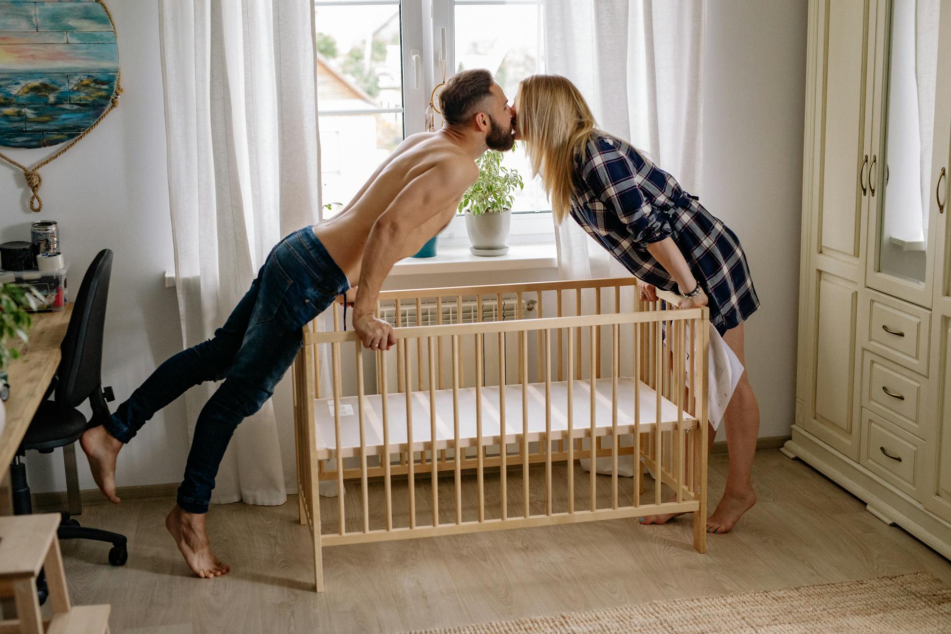 Un couple qui s'embrasse en installant un berceau de bébé | Source : Pexels