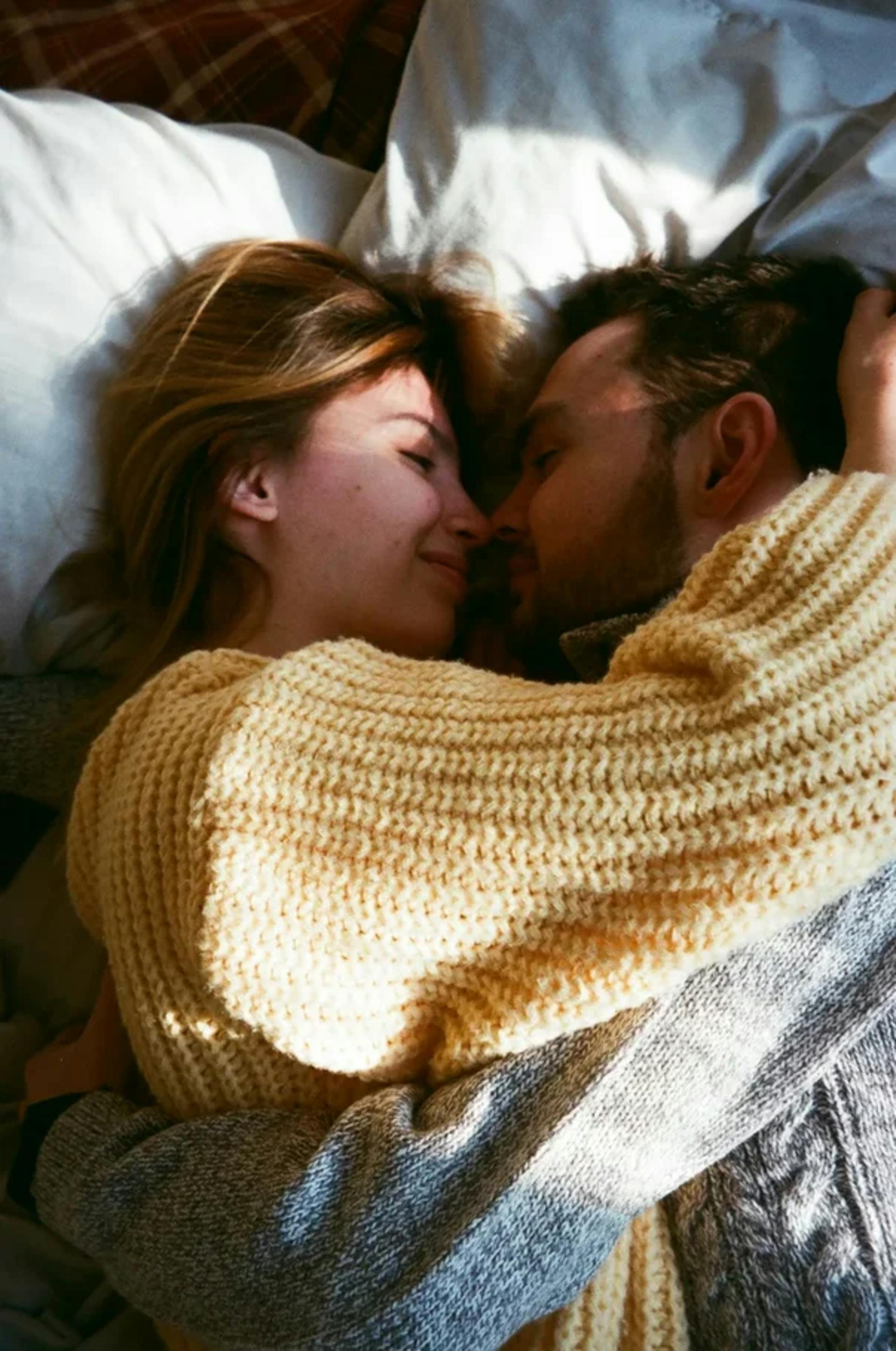 Un couple heureux en pull-over allongé et enlacé sur un lit | Source : Pexels