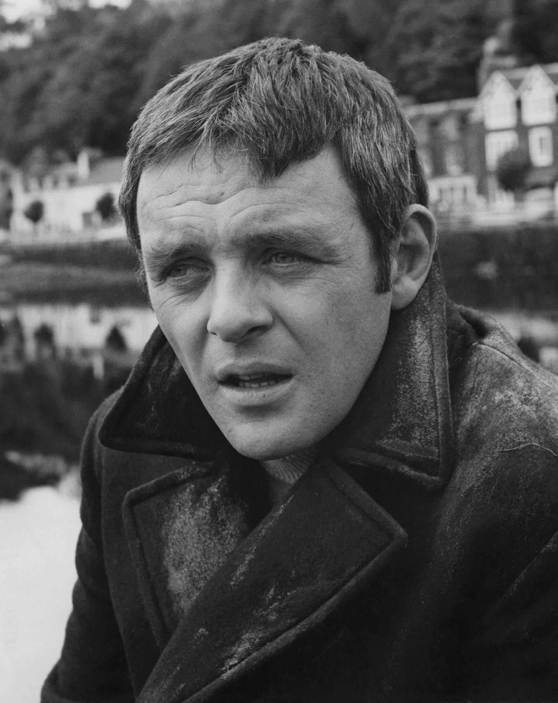 Le regard perdu dans le lointain, Anthony Hopkins affiche une expression à mi-chemin entre la contemplation et une triste mélancolie. Le manteau texturé et le fond brumeux évoquent une atmosphère de solitude et de réflexion. Chaque détail de cette scène monochrome traduit la profondeur, la retenue et le poids des émotions inexprimées.