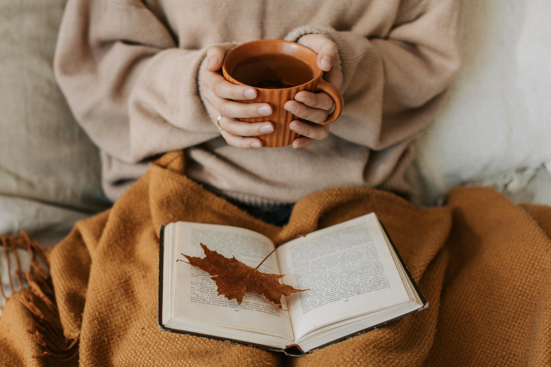 Gros plan sur une femme qui lit un livre en tenant une tasse de thé | Source : Pexels