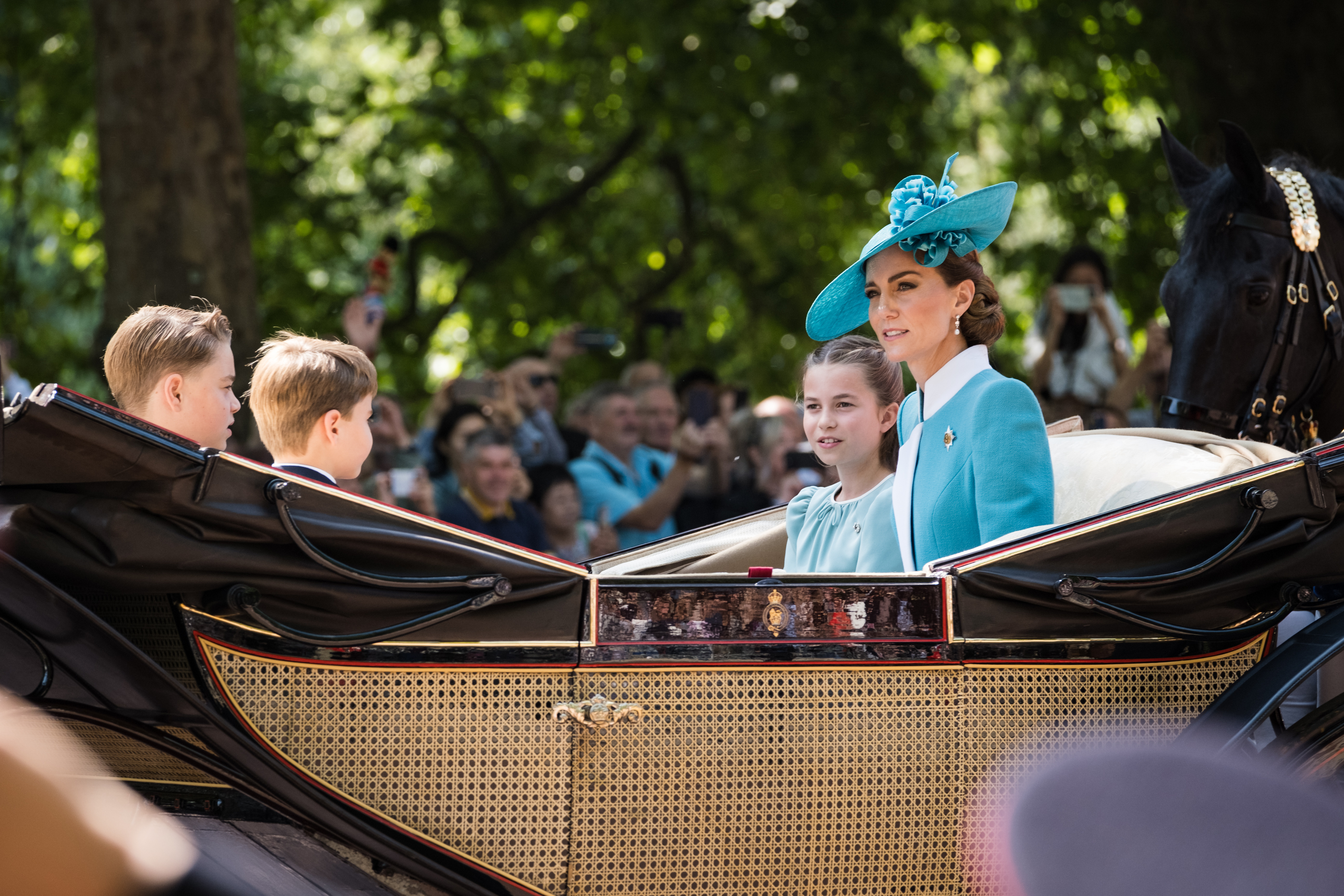 La princesse Charlotte, la princesse Catherine, le prince George et le prince Louis montent dans le carrosse royal tandis que les gens regardent et prennent des photos de la mère avec ses enfants.