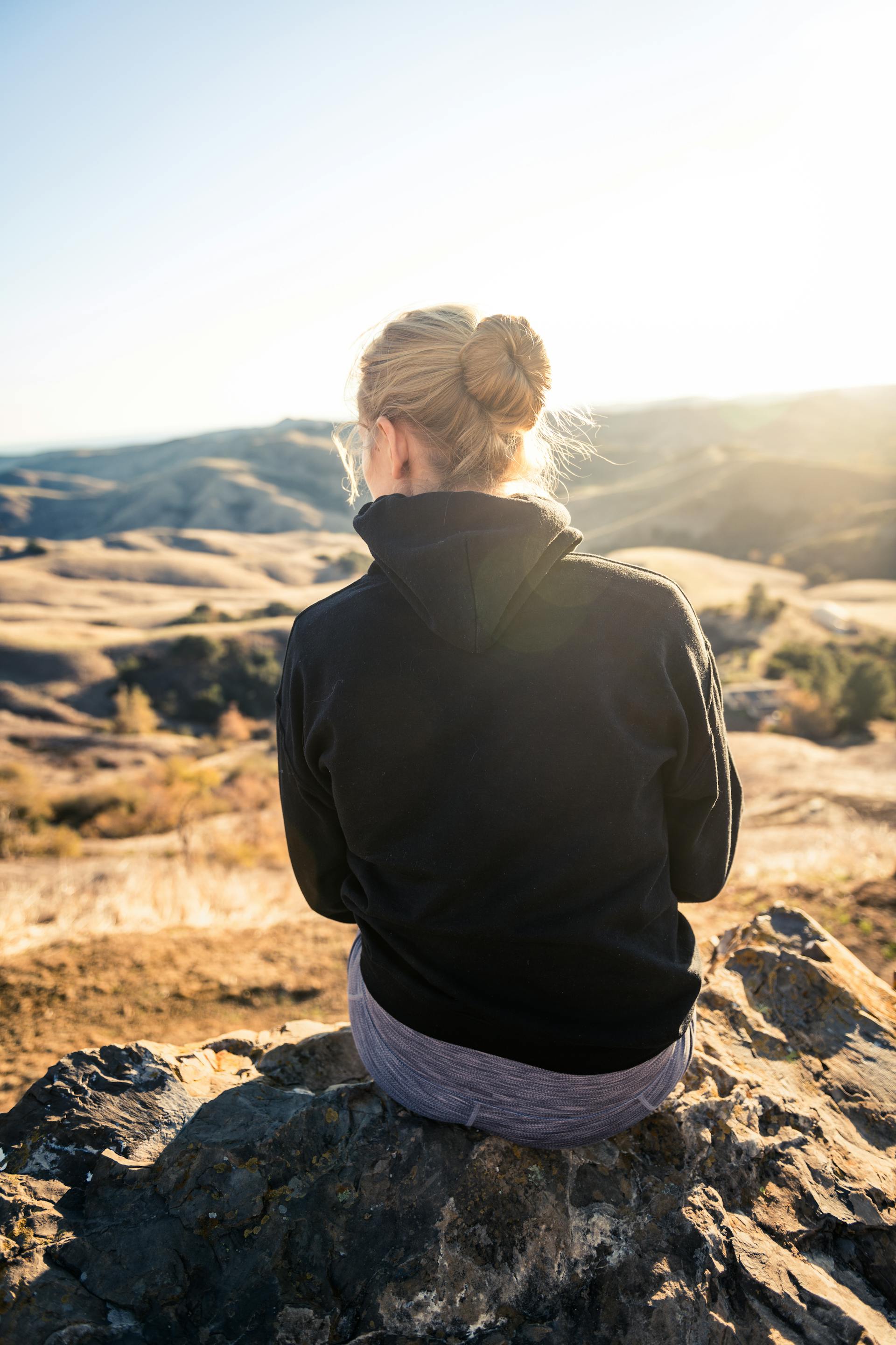 Femme en sweat à capuche noir assise sur un rocher | Source : Pexels