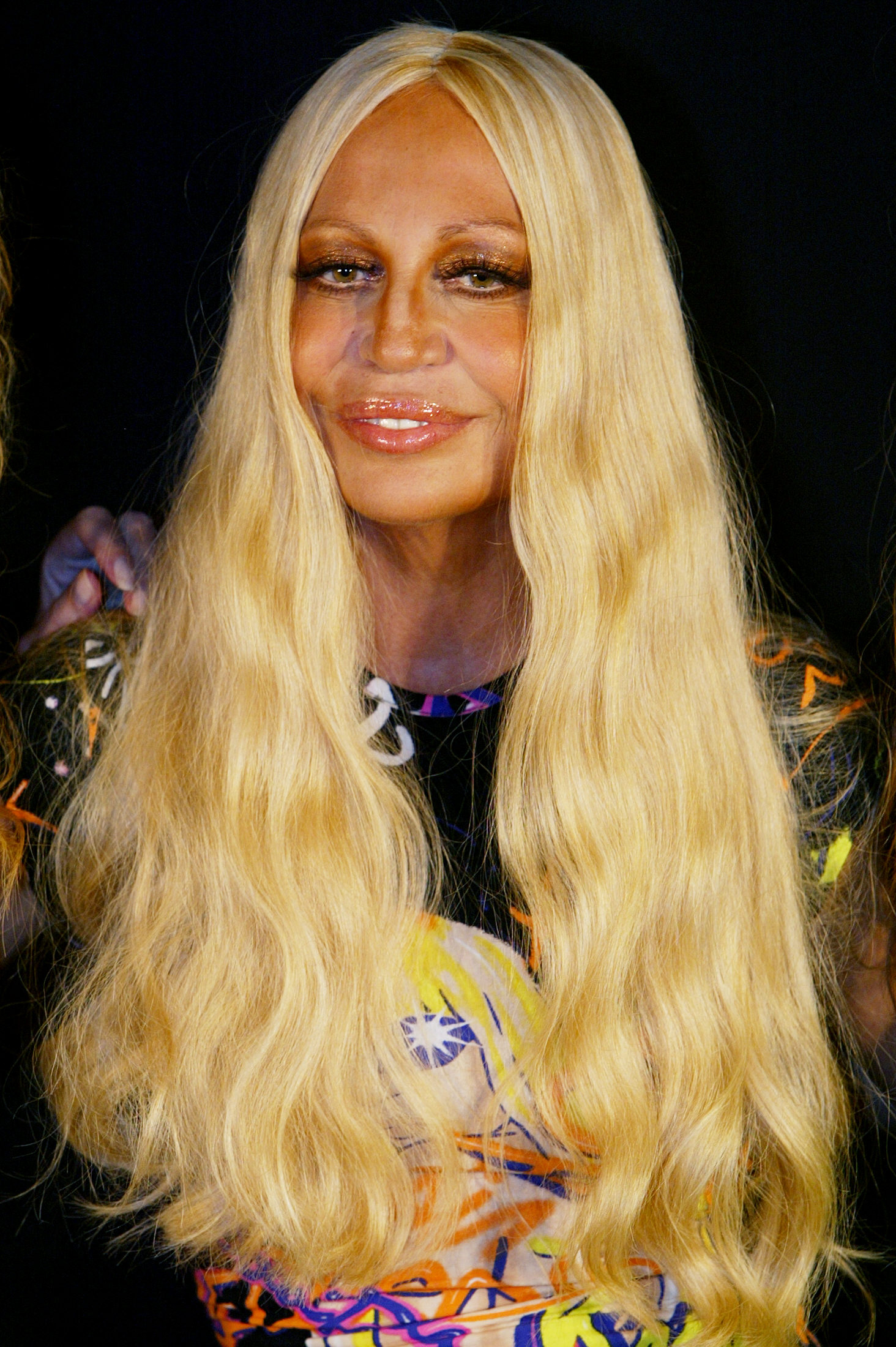 Donatella Versace, 48 ans, souriait avant le défilé de Gianni Versace le 4 octobre 2003 à Milan, en Italie. Son visage affichait une tension extrême, des lèvres fortement augmentées et brillantes, et un teint profondément bronzé.