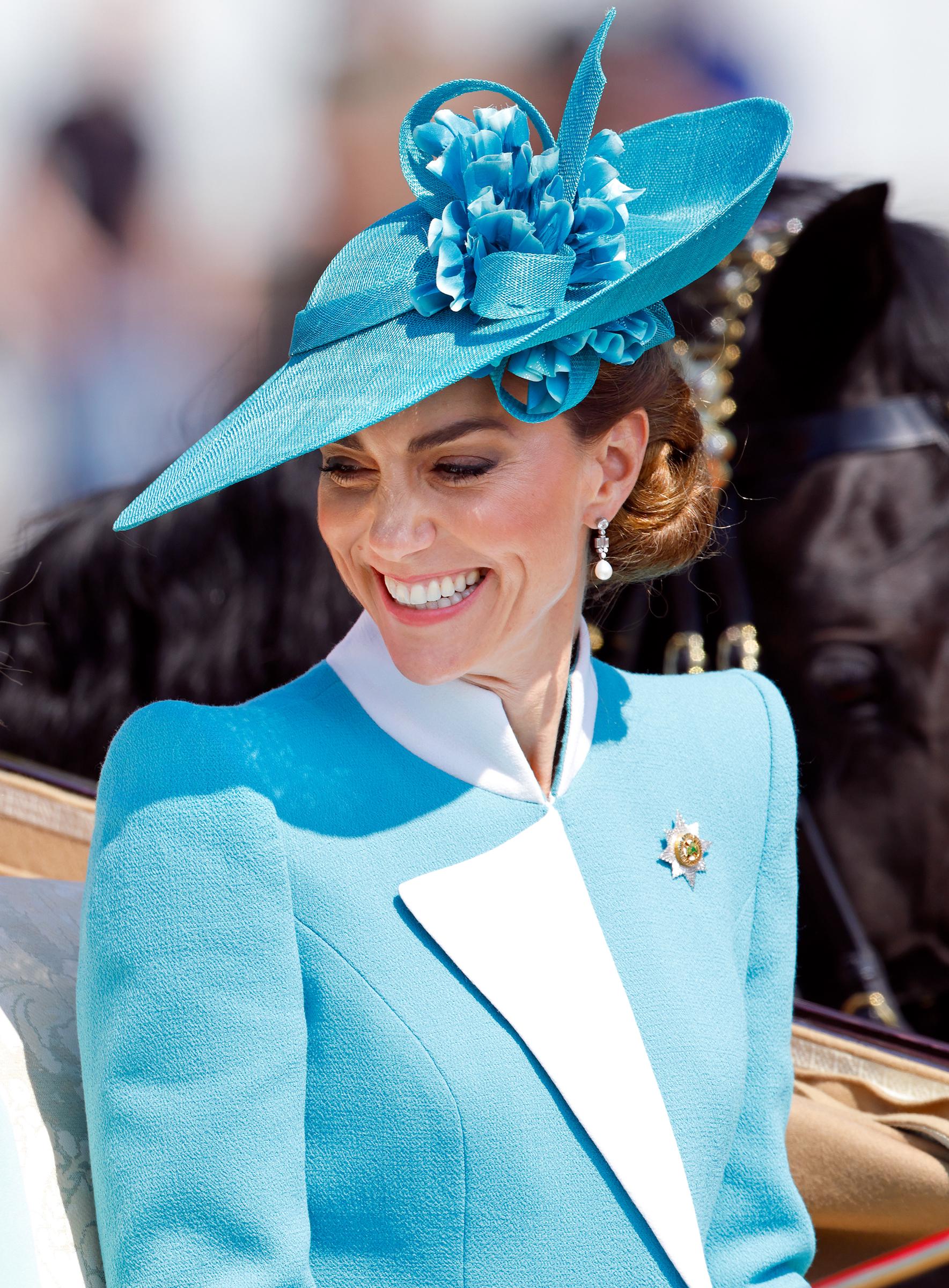 Dans un gros plan pris lors de son arrivée en calèche au Trooping the Colour 2025, la princesse Catherine sourit chaleureusement à la foule rassemblée. Son expression rayonne d'une confiance sereine, soulignée par les délicats motifs floraux de son chapeau bleu sarcelle et l'élégance impeccable de sa tenue, une image de grâce dans le respect de la tradition.