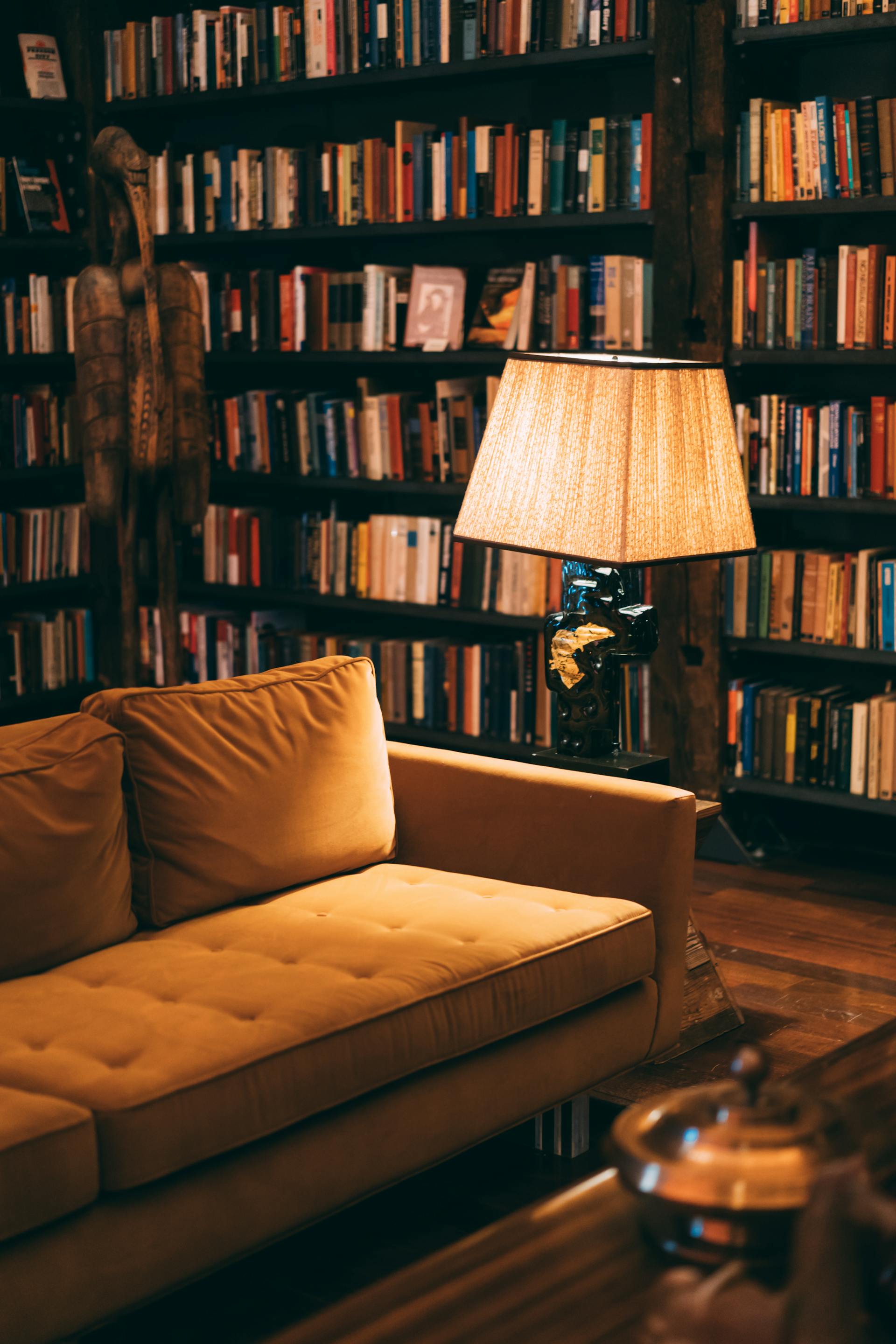 Une lampe placée à côté d'un canapé dans une bibliothèque à domicile | Source : Pexels