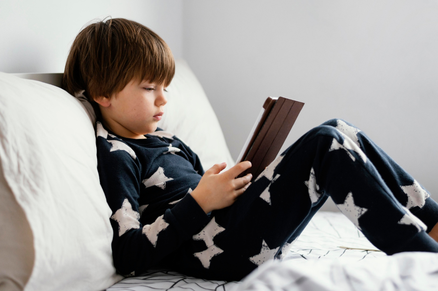 Un garçon assis sur un lit avec sa tablette numérique | Source : Freepik