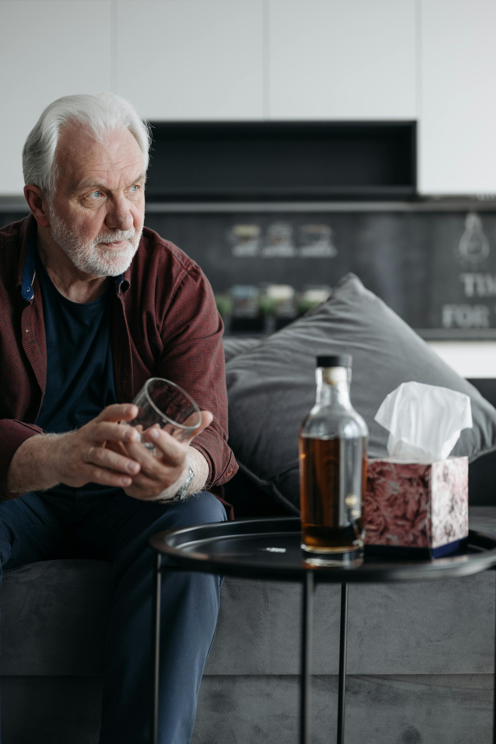 Un homme tenant un verre avec une bouteille de bière posée devant lui | Source : Pexels