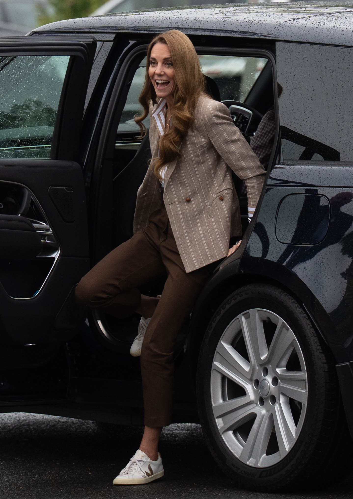 La princesse Catherine sort d'un SUV noir sous un ciel couvert pour se rendre à l'hôpital de Colchester. Vêtue d'un pantalon couleur terre, de baskets et d'un blazer à fines rayures, elle arrive prête à se mettre au travail, au sens propre comme au figuré.