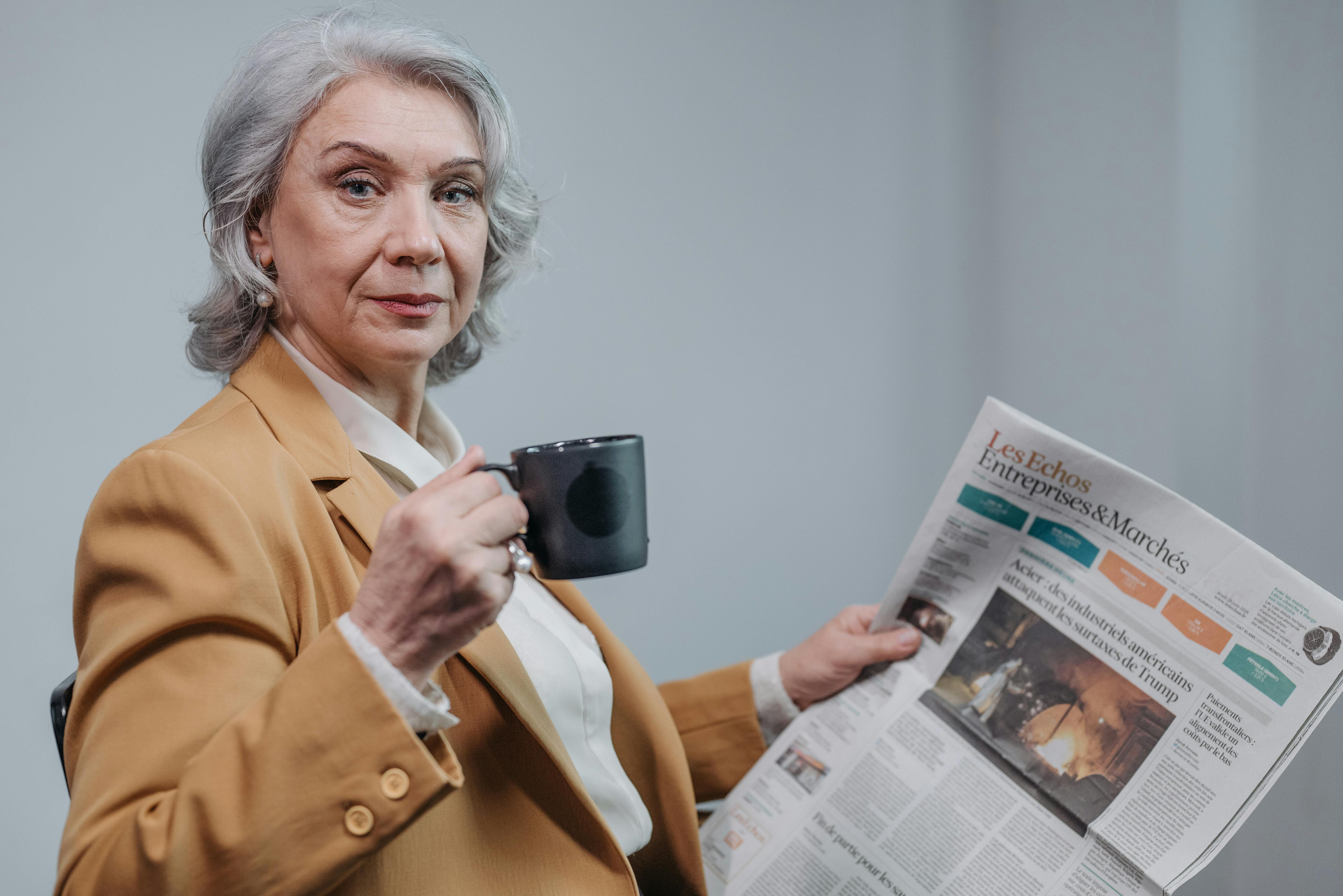 Une femme sérieuse prenant un café et lisant un journal | Source : Pexels