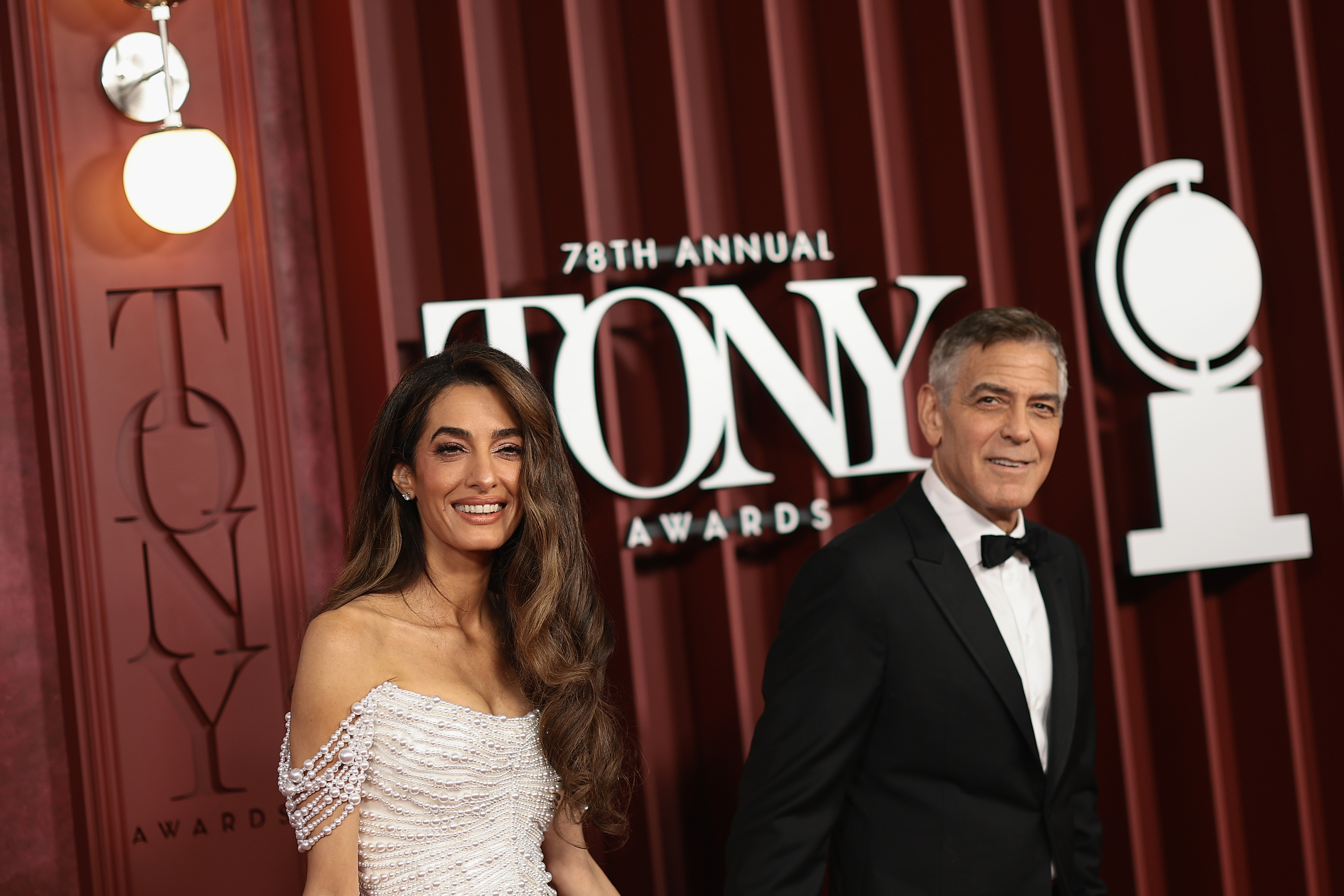 George et Amal Clooney sourient côte à côte alors qu'ils posent près de l'enseigne de la 78e édition des Tony Awards. La présence confiante du couple ajoute une touche de charme hollywoodien à la grande soirée de Broadway.