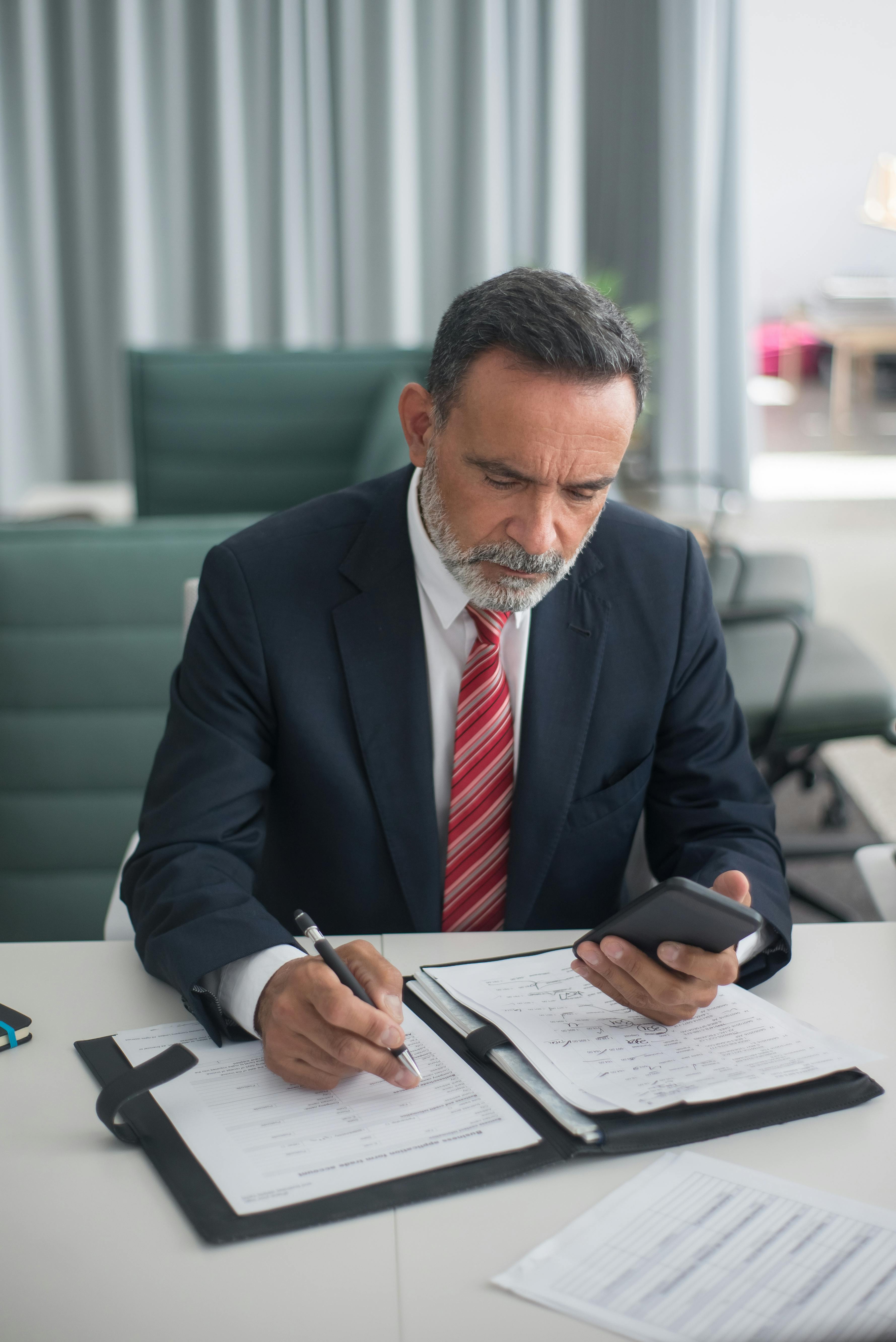 Un homme tenant son téléphone tout en écrivant quelque chose | Source : Pexels