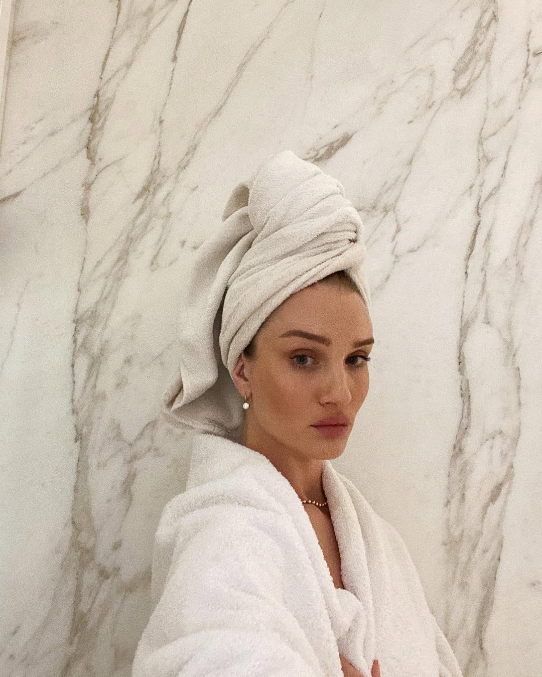 Rosie Huntington-Whiteley pose dans une salle de bain sereine en marbre, enveloppée dans un peignoir blanc en peluche avec un turban de serviette assorti. | Source : Instagram/rosiehw