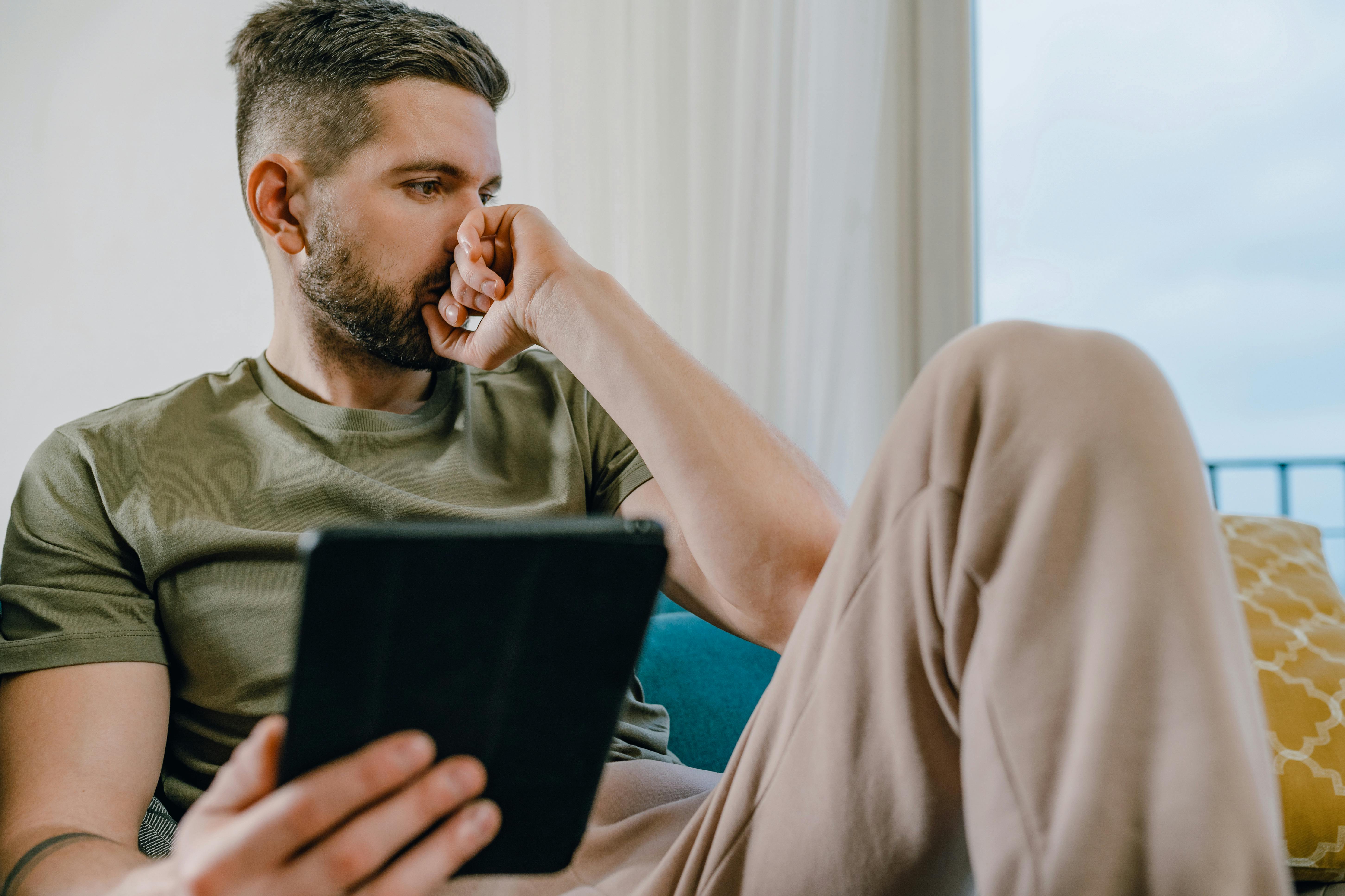 Un homme plongé dans ses pensées, tenant une tablette | Source : Pexels