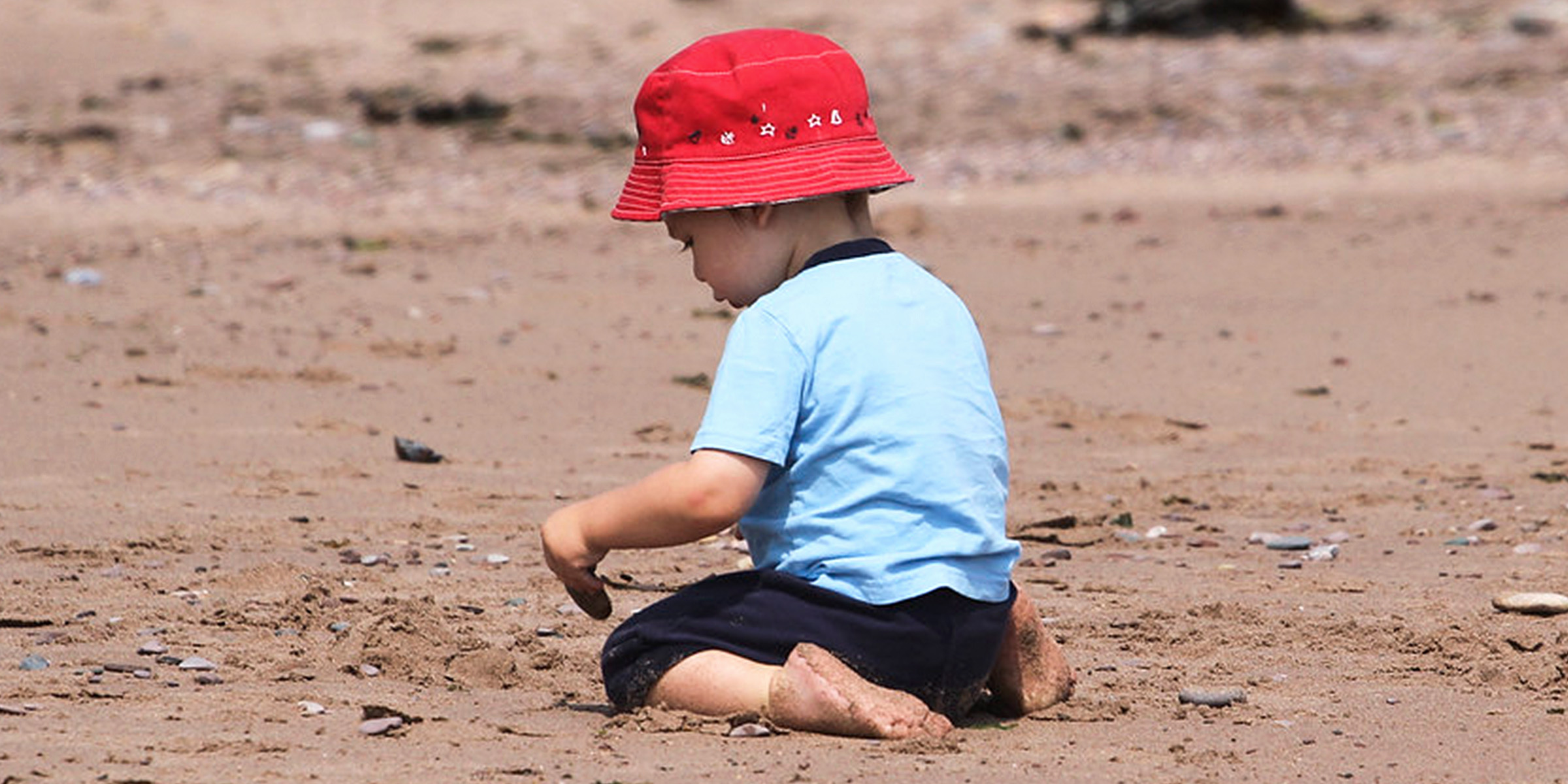 Un petit garçon assis sur le sable | Source : Flickr