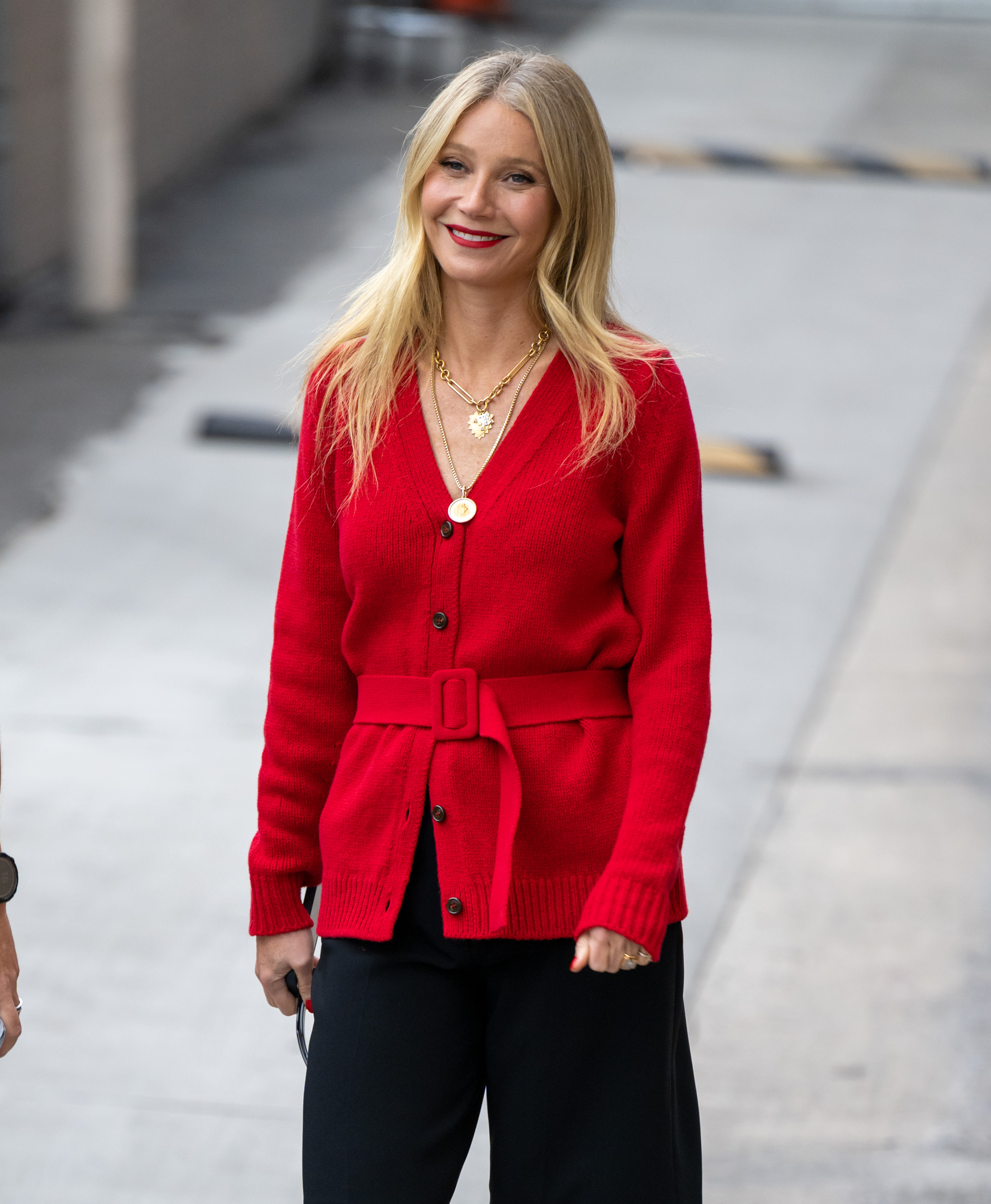 Gwyneth Paltrow arrive à l'émission « Jimmy Kimmel Live » à Los Angeles, en Californie, le 31 octobre 2022. Elle porte un cardigan rouge ceinturé sur un pantalon noir, associé à plusieurs colliers en or pour une touche de brillance. Ses cheveux blonds sont coiffés en boucles lâches avec une raie au milieu, tandis que son rouge à lèvres rouge vif ajoute une touche de couleur éclatante à son look.