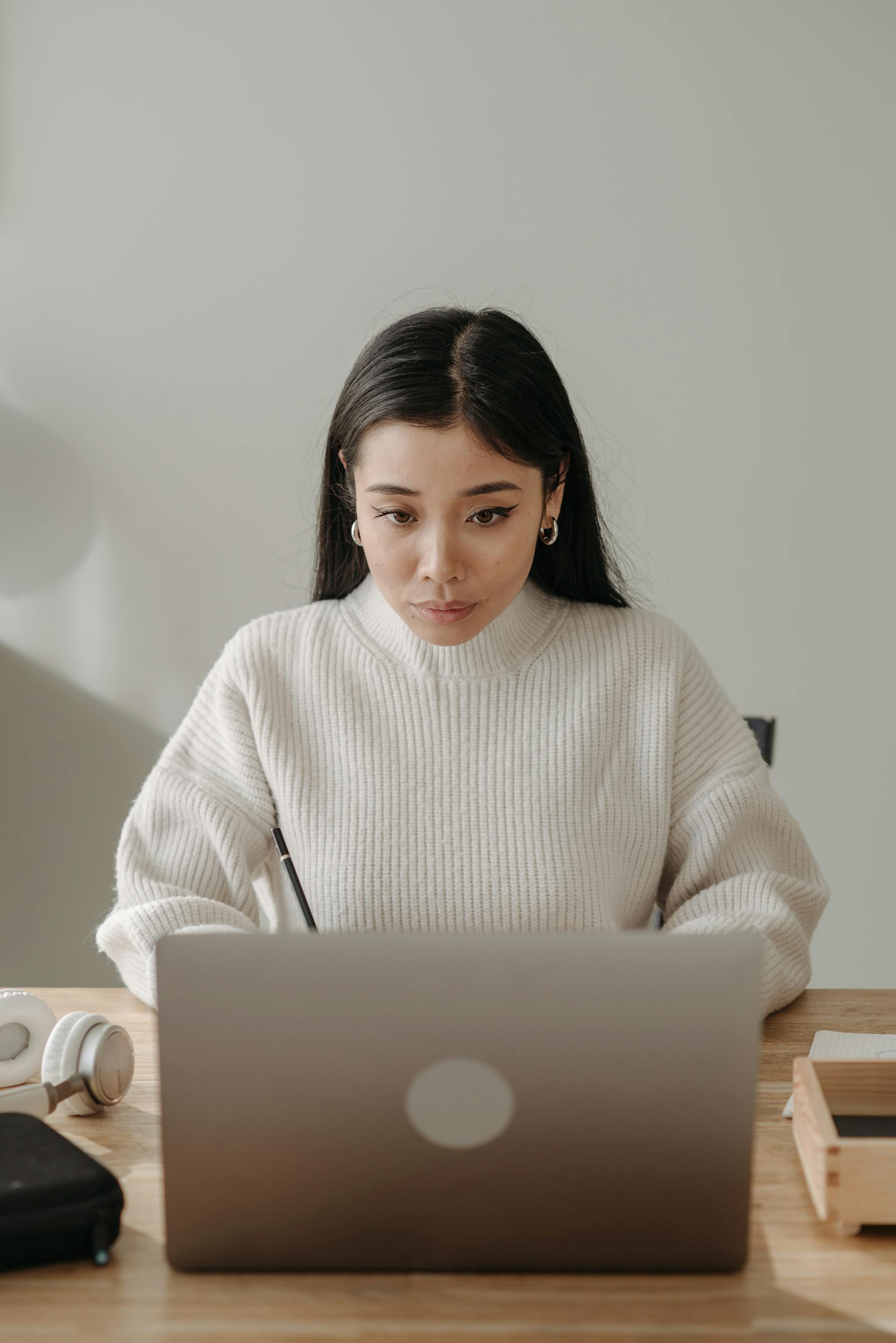 Une femme aux cheveux noirs portant un pull blanc regarde attentivement un ordinateur portable | Source : Pexels