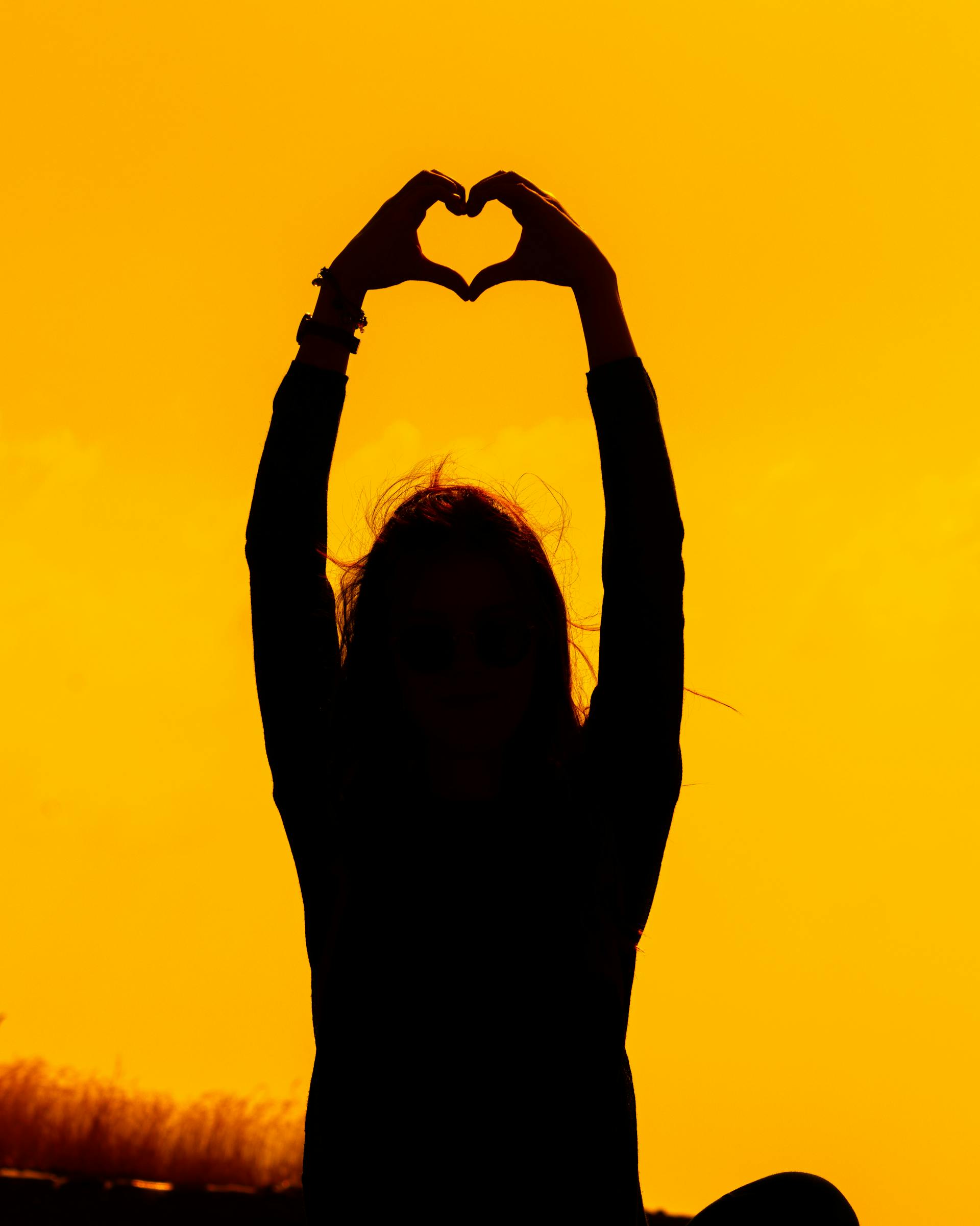 Silhouette d'une femme formant un cœur avec ses mains au coucher du soleil | Source : Pexels
