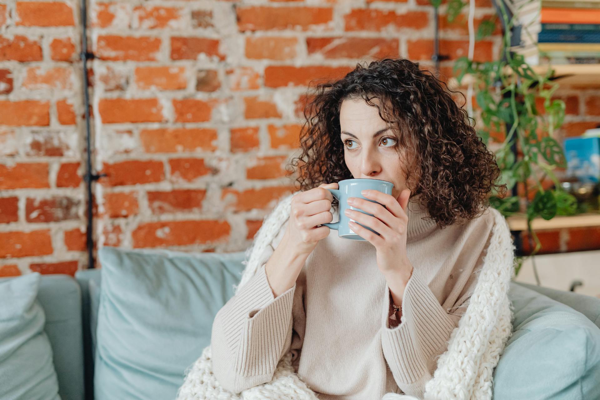 Une femme buvant une boisson chaude sur un canapé | Source : Pexels