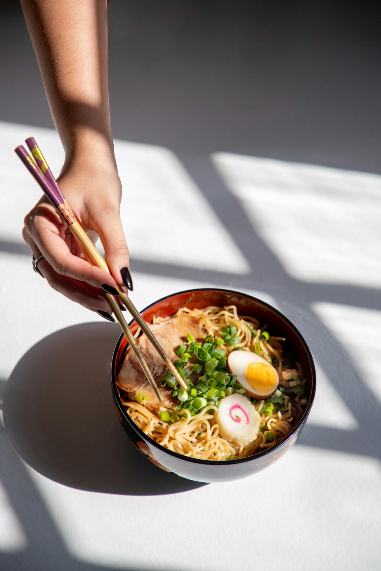 Une femme tenant des baguettes et mangeant des ramen | Source : Pexels