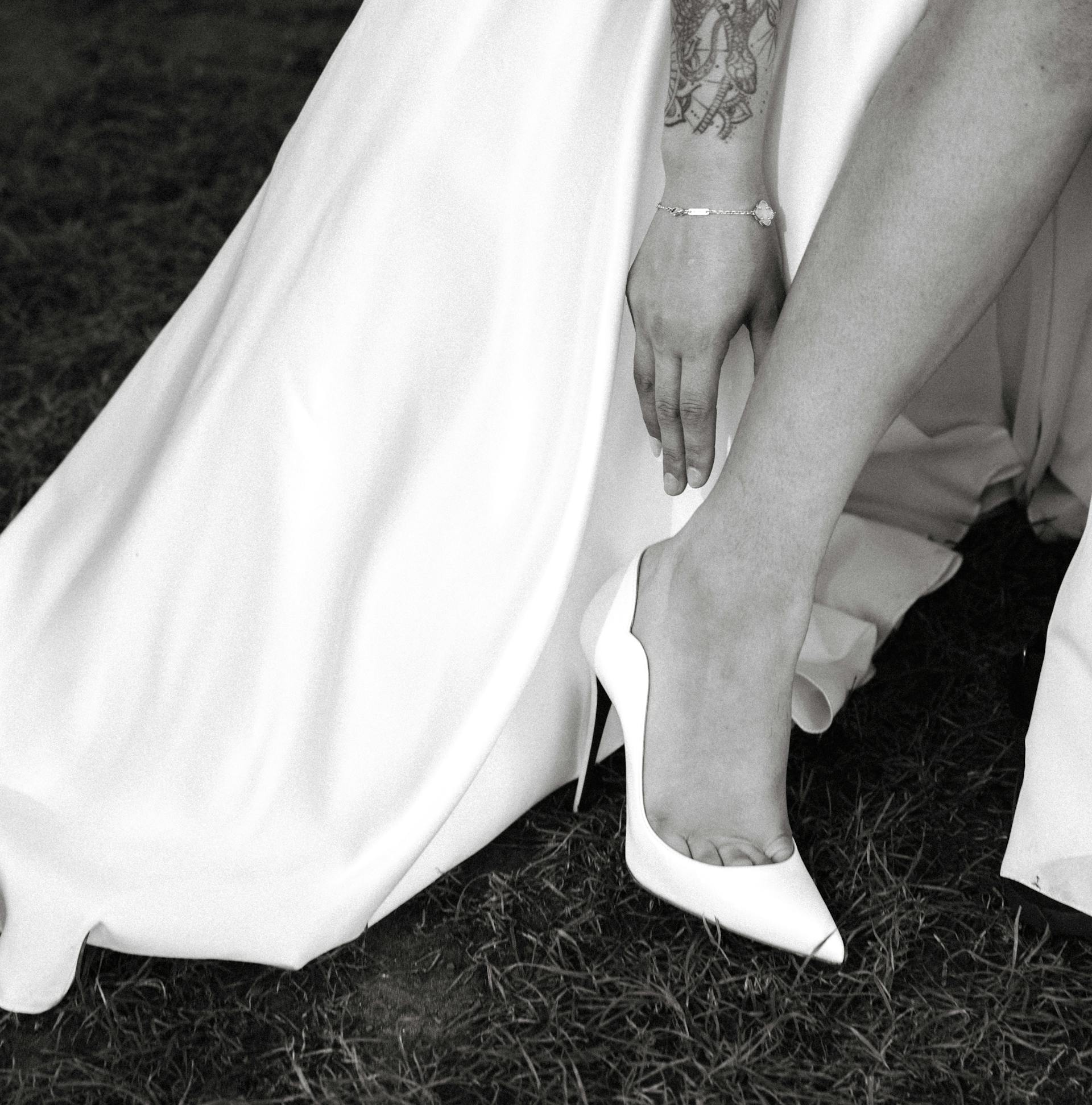 Un gros plan d'une mariée qui attrape ses talons alors qu'elle se tient debout sur l'herbe | Source : Pexels