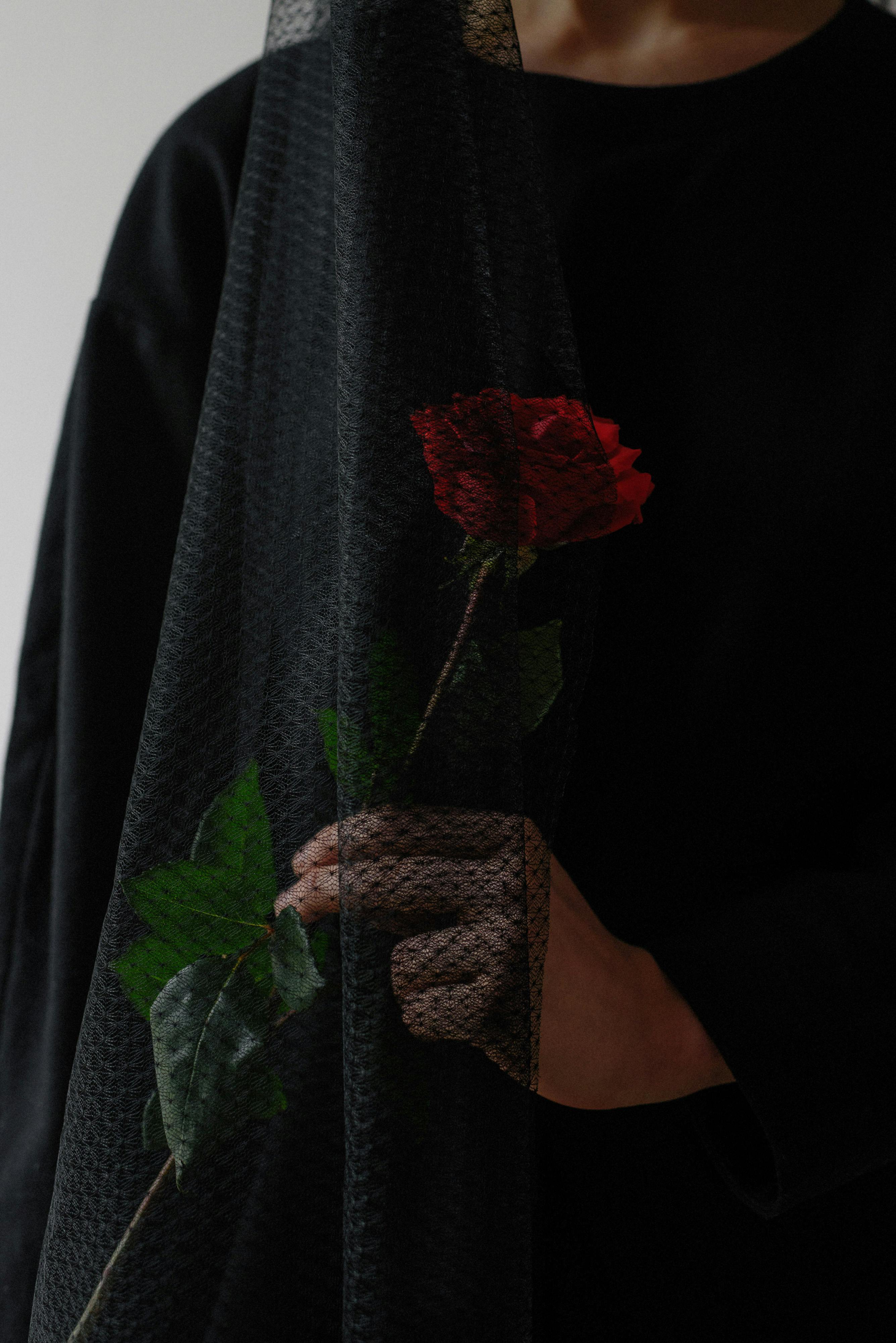 Une femme vêtue de noir tenant une rose rouge | Source : Pexels