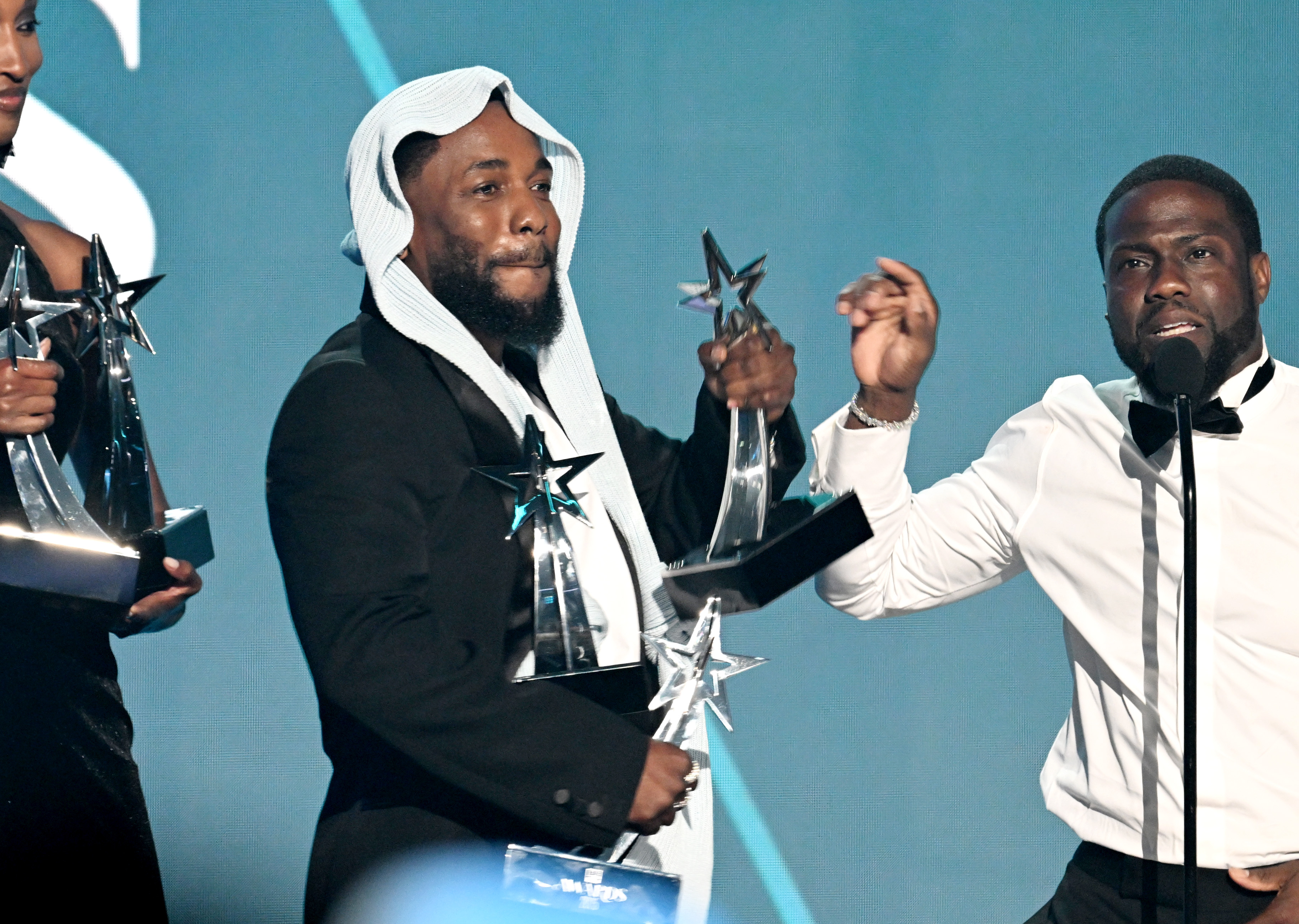 Kendrick Lamar se tient aux côtés de l'humoriste Kevin Hart, jonglant avec plusieurs de ses cinq trophées des BET Awards. L'échange humoristique a suivi le discours émouvant de Lamar et s'est déroulé en direct sur la scène des BET Awards 2025 à Los Angeles.