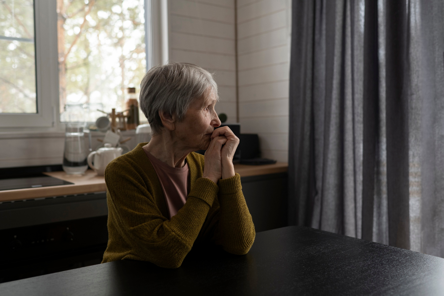 Une femme âgée pensive assise à une table | Source : Freepik