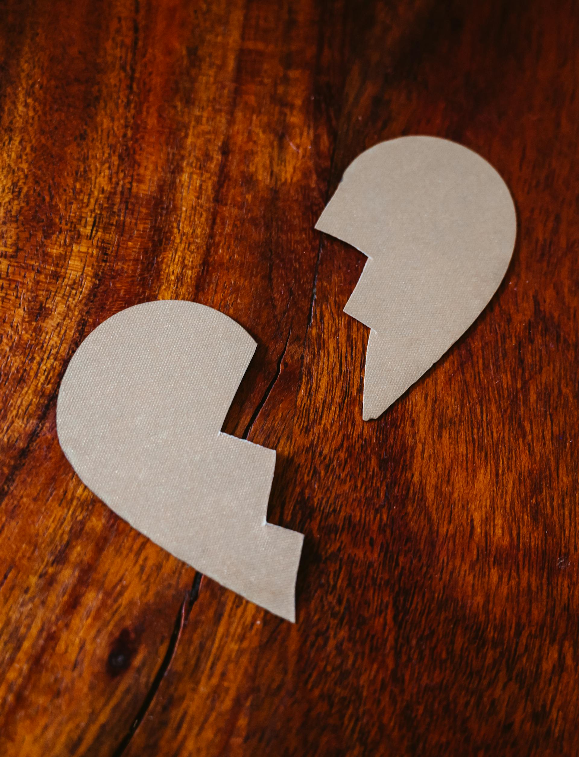 Des pièces en carton représentant un cœur brisé sur une surface en bois | Source : Pexels