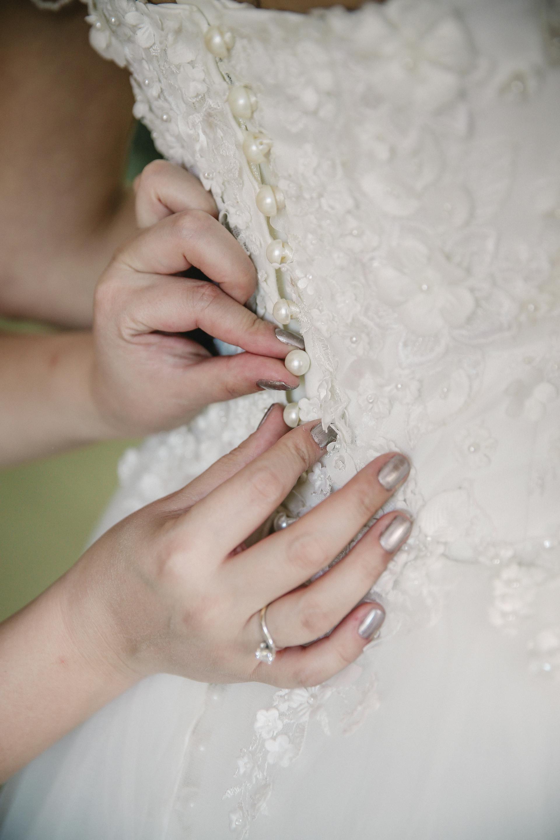 Des mains qui boutonnent une robe de mariée | Source : Pexels