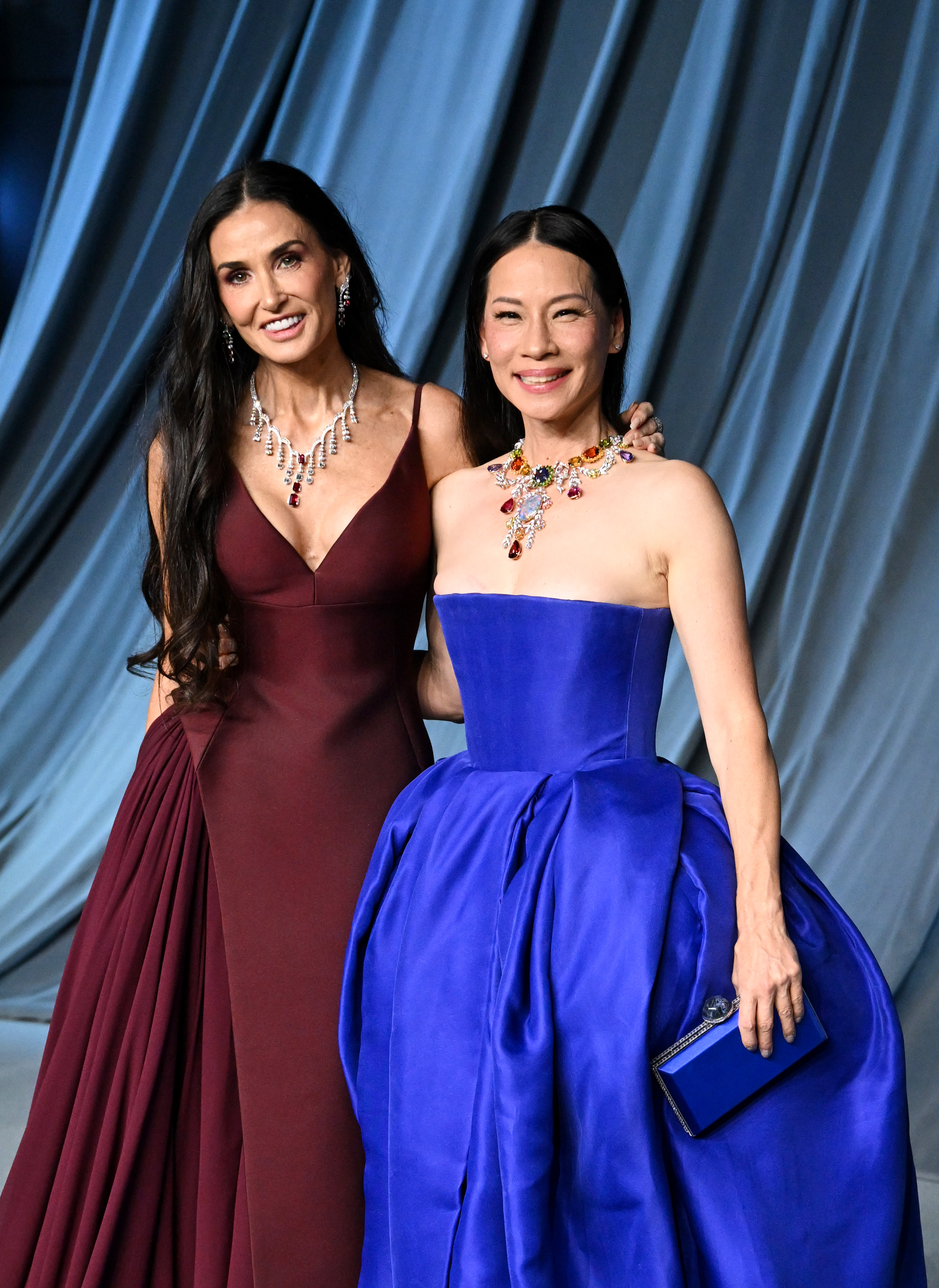 Souriant naturellement aux côtés de Lucy Liu, Demi Moore rayonne d'un glamour décontracté dans sa robe bordeaux qui épouse ses courbes, tandis que Liu éblouit dans une robe bleu roi avec un décolleté orné de bijoux éclatants — un véritable moment de duo puissant.
