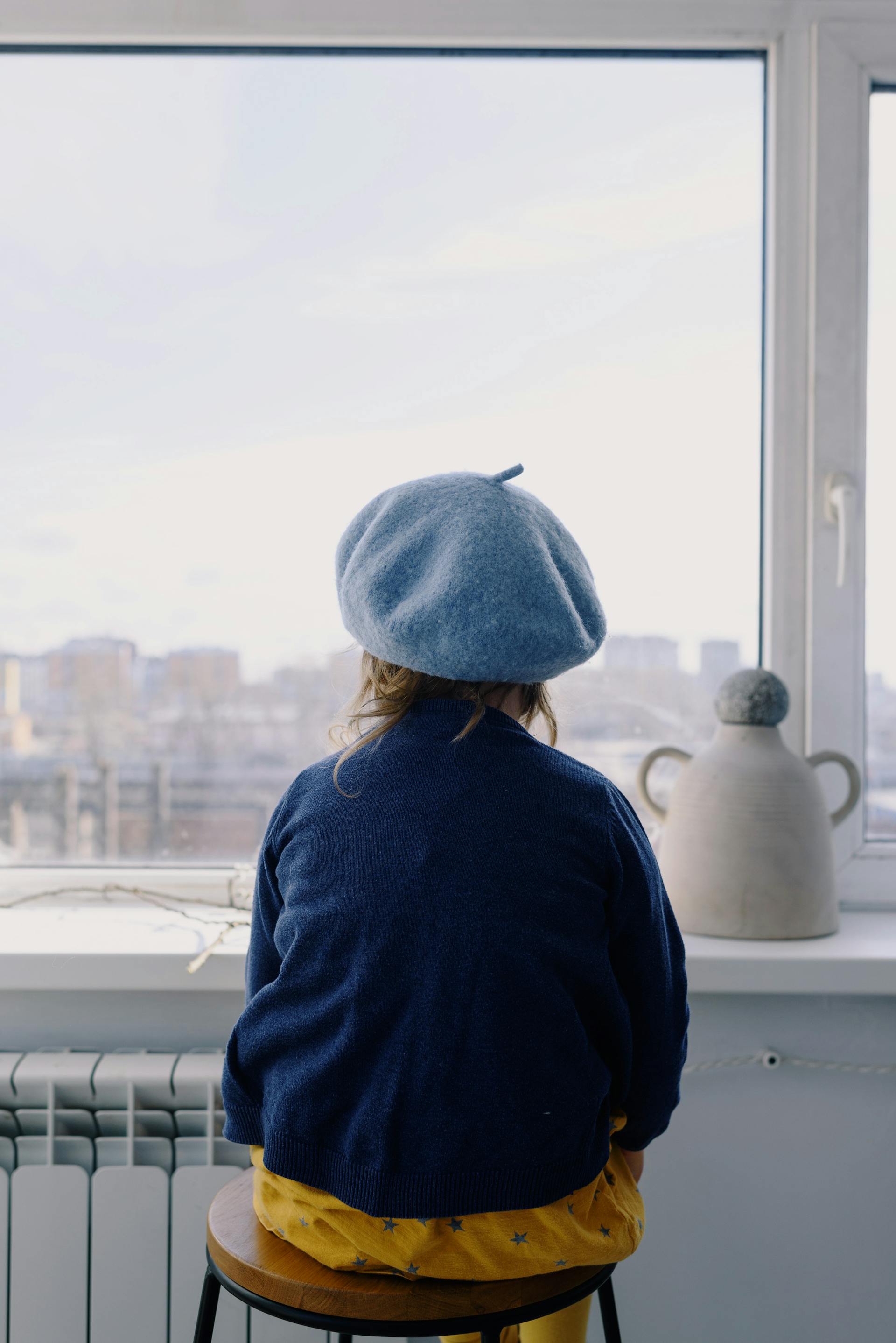 Une petite fille coiffée d'un béret qui regarde dehors depuis la fenêtre | Source : Pexels