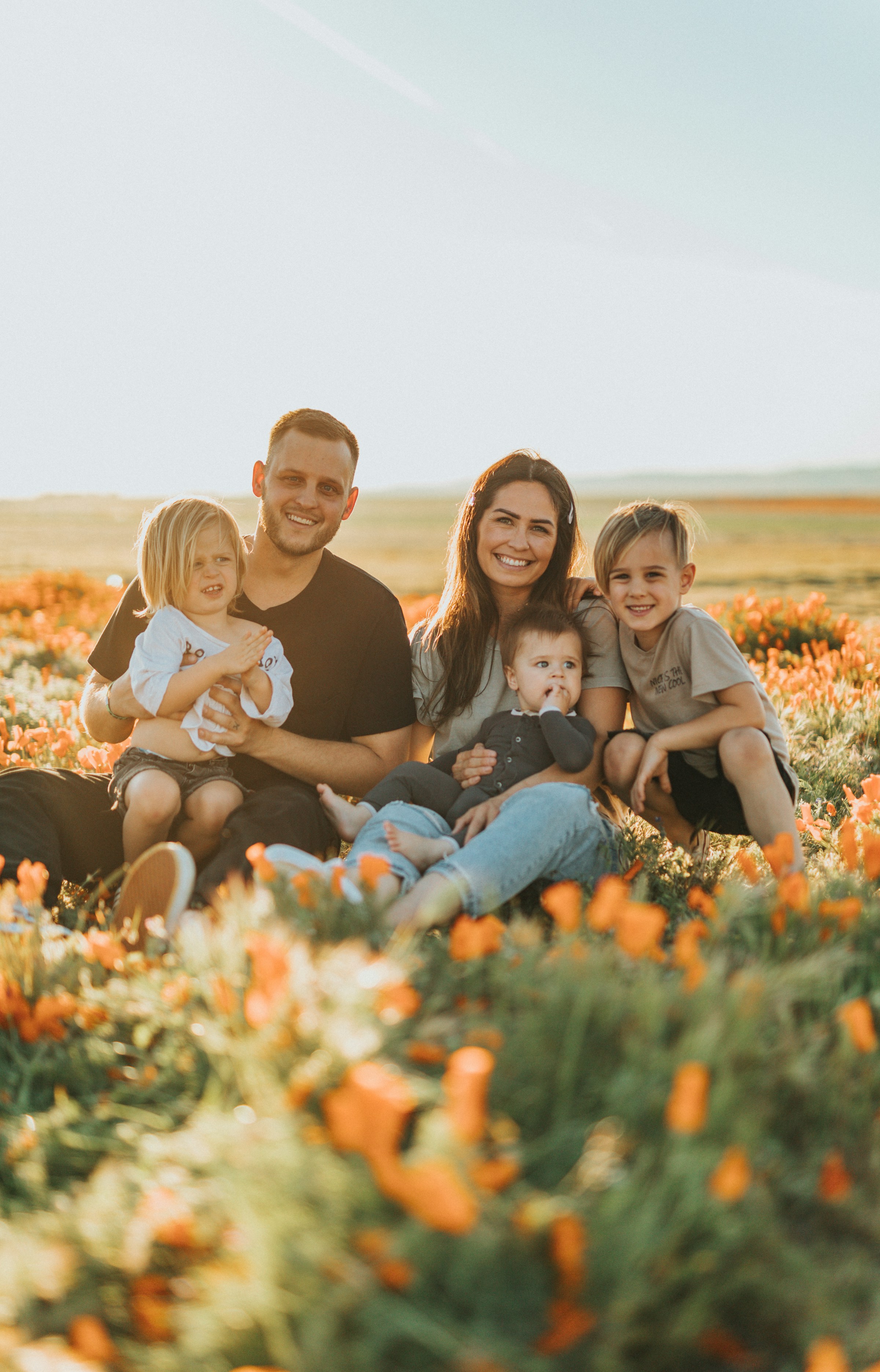 Un couple heureux avec leurs trois enfants assis ensemble dans un champ verdoyant | Source : Unsplash