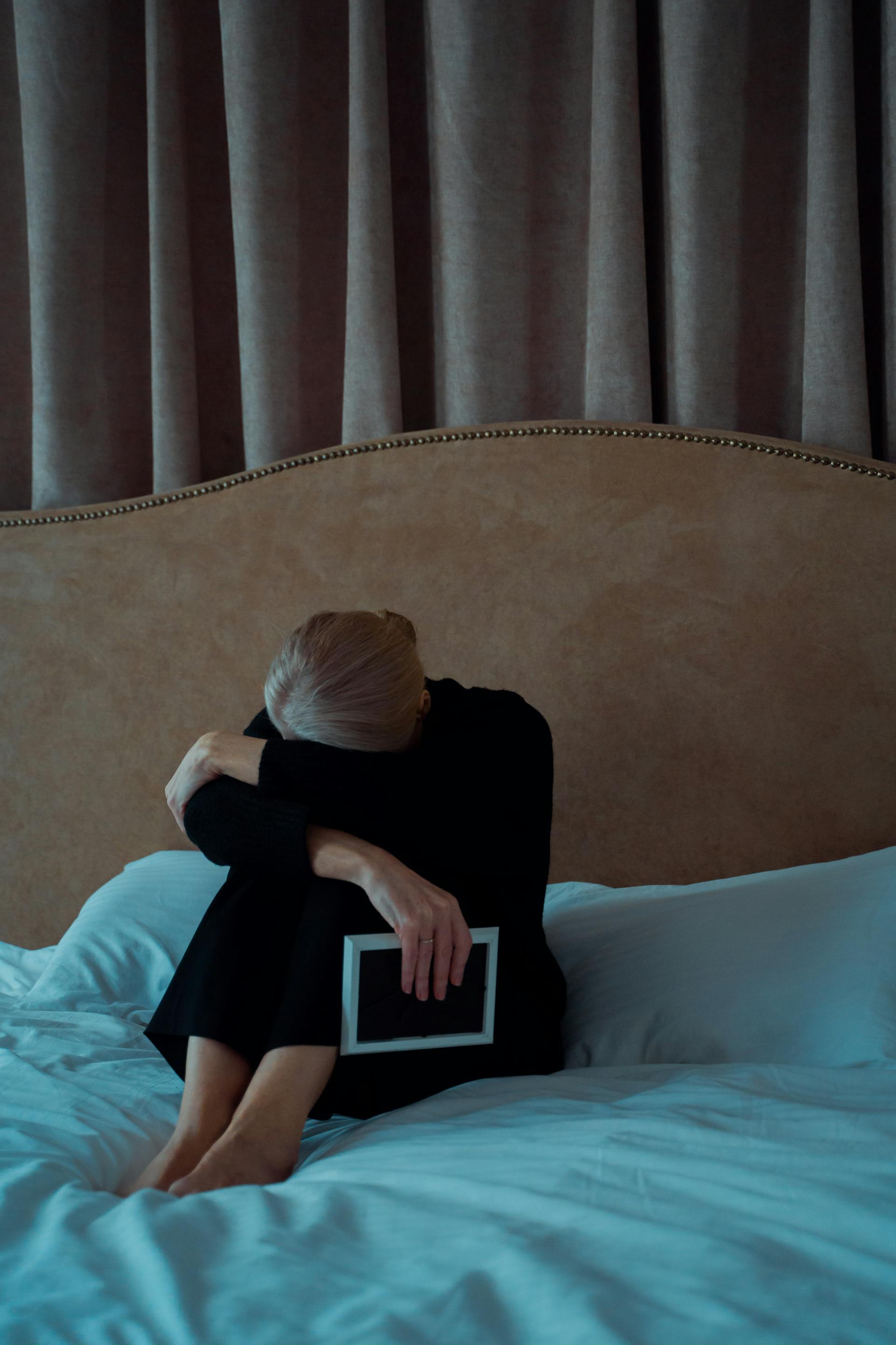 Une femme âgée triste tenant un cadre photo alors qu'elle est assise sur son lit | Source : Pexels