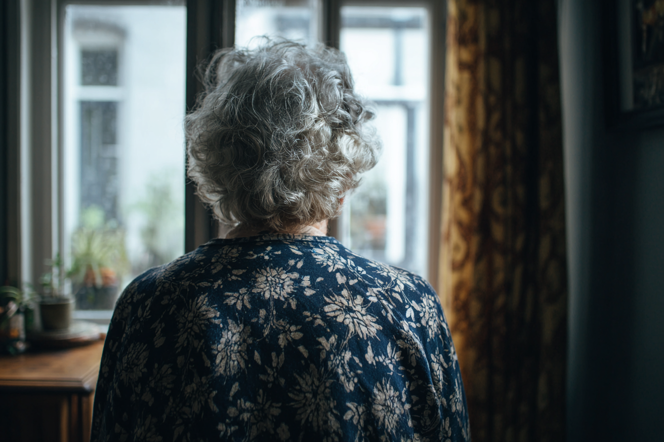 Une femme âgée debout près d'une fenêtre | Source : Midjourney