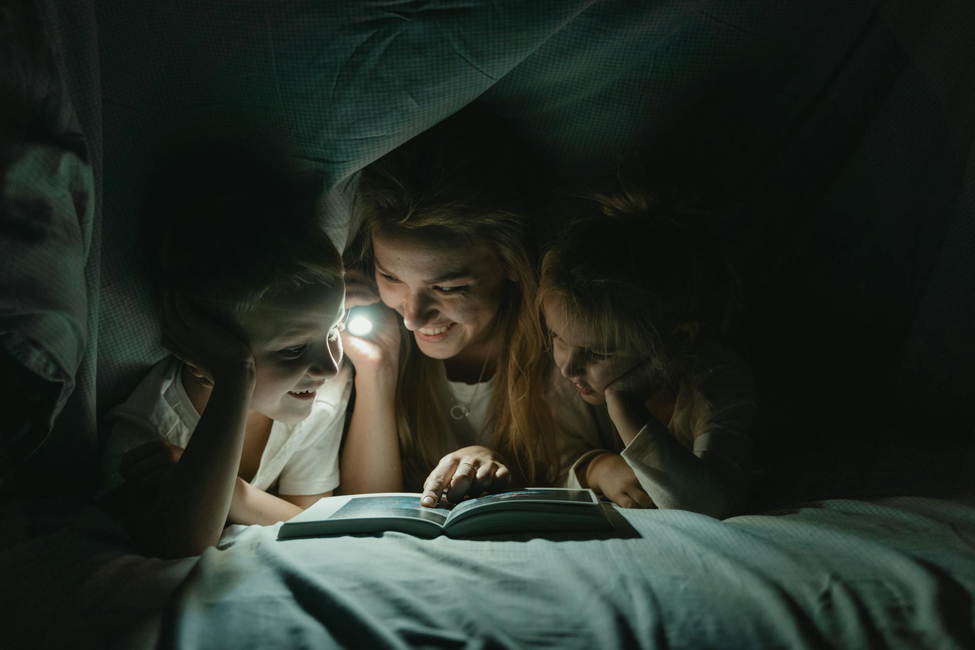 Une femme tenant une lampe de poche et lisant une histoire à ses enfants | Source : Pexels