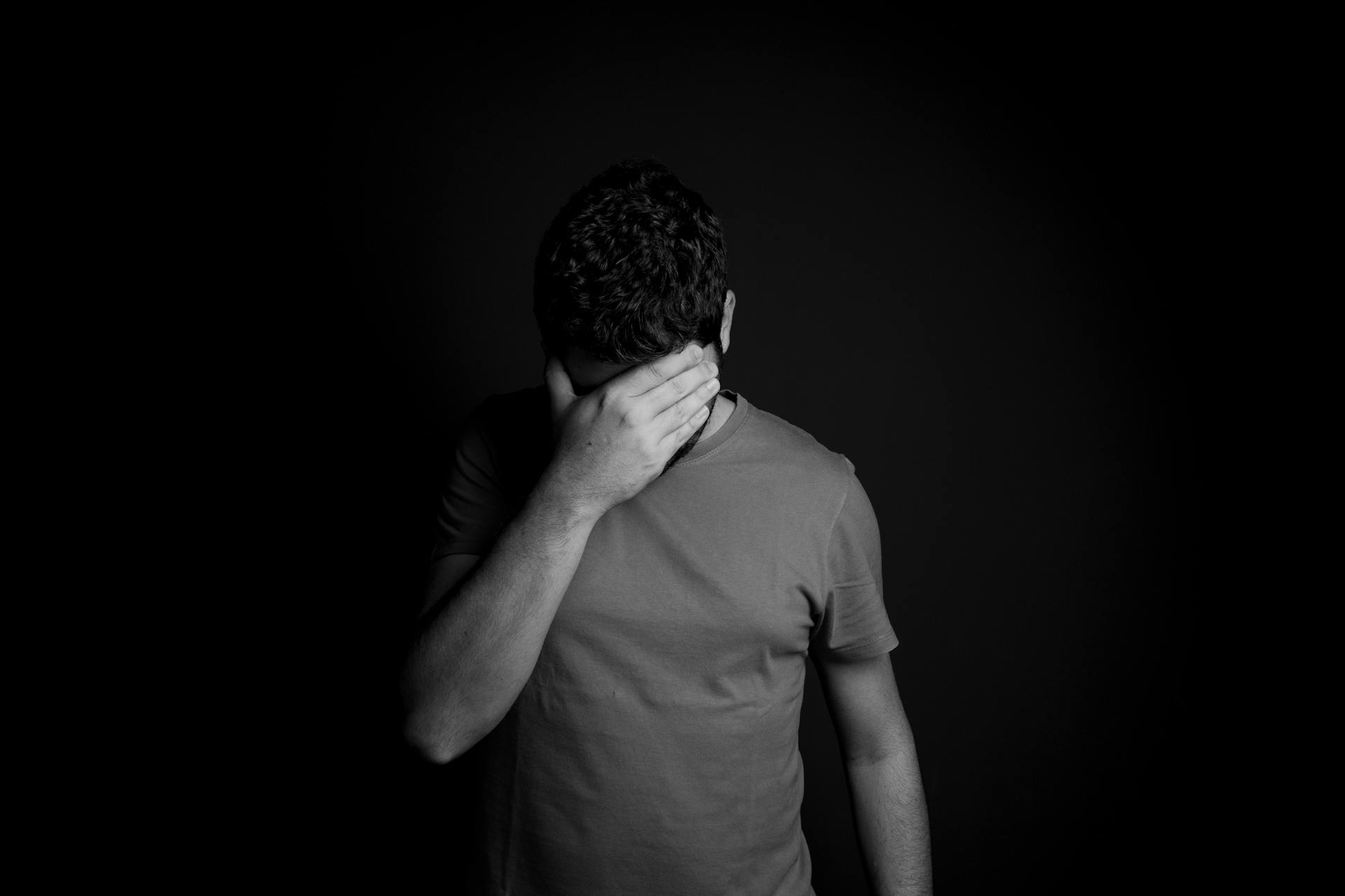 Une photo en niveaux de gris d'un homme triste qui se couvre le visage avec sa main | Source : Pexels