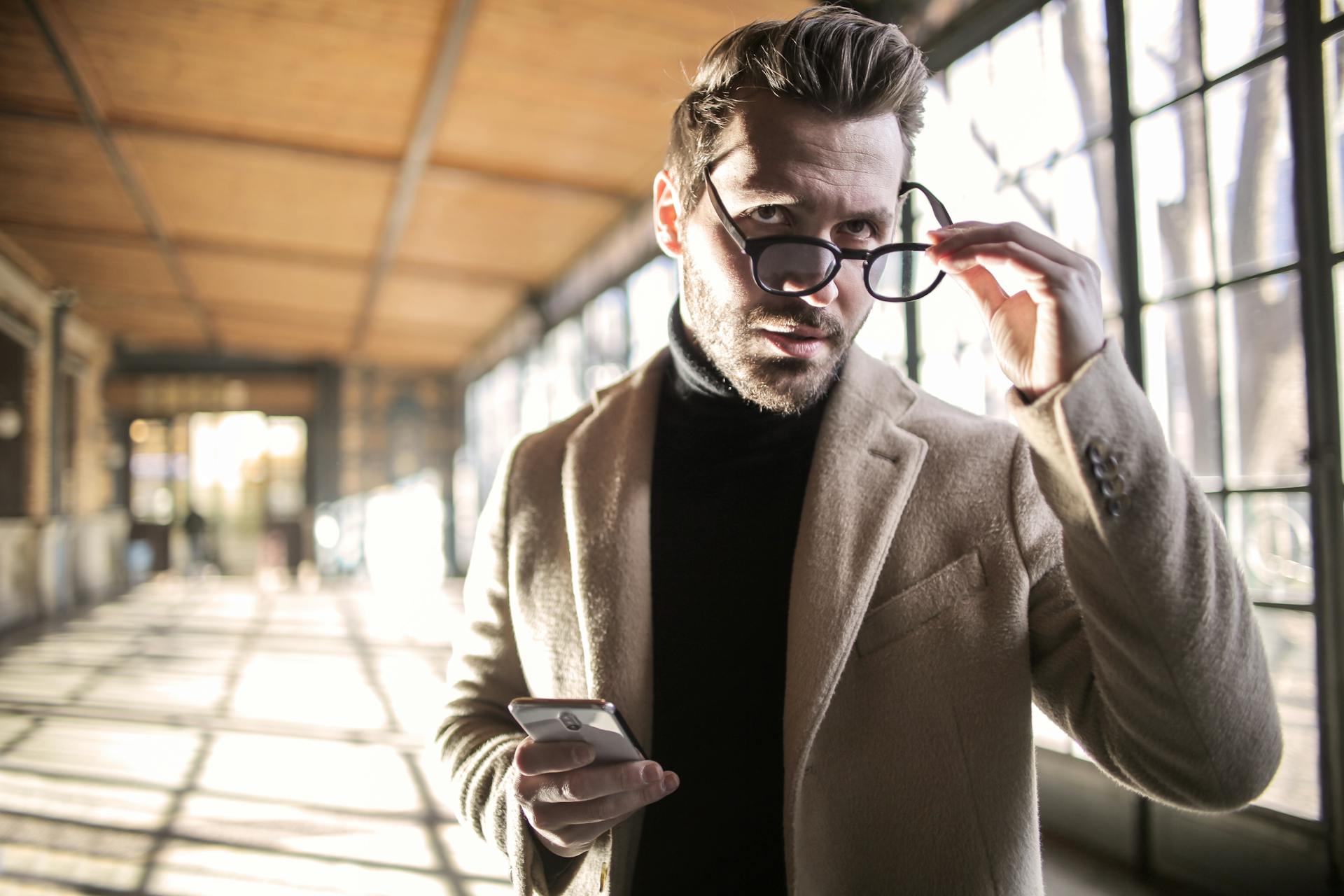 Un homme tient un téléphone dans une main et ses lunettes dans l'autre | Source : Pexels